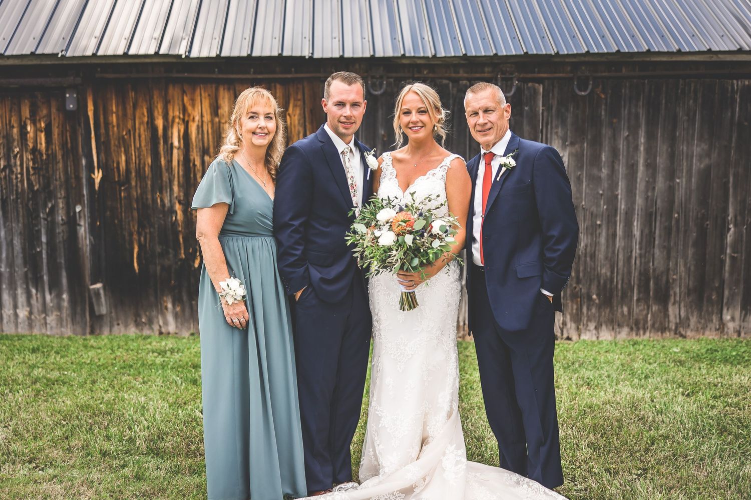 Wedding group photo featuring attendants in blue dresses against a wooden barn setting.