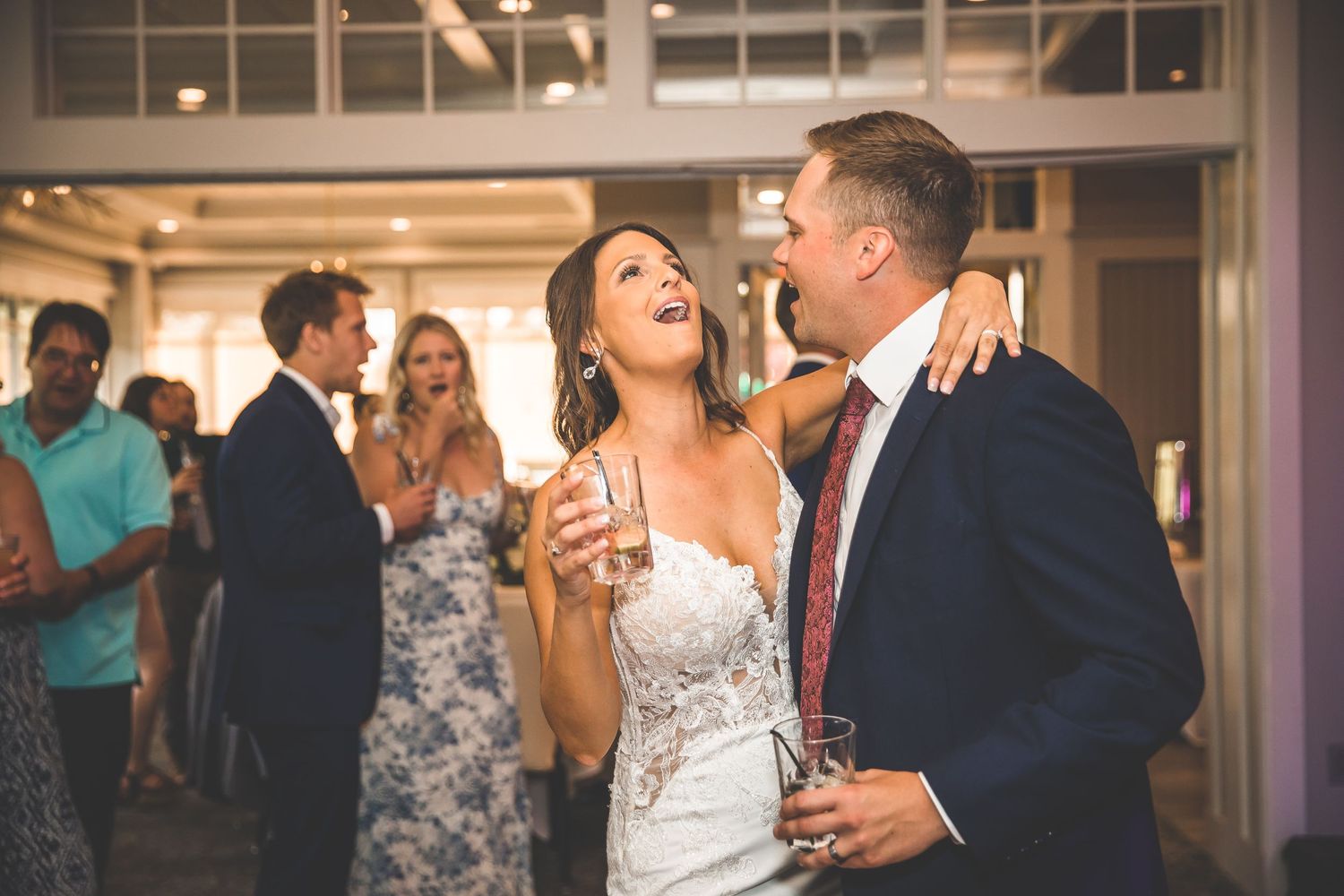 Wedding couple shares romantic moments during indoor reception with guests in background.