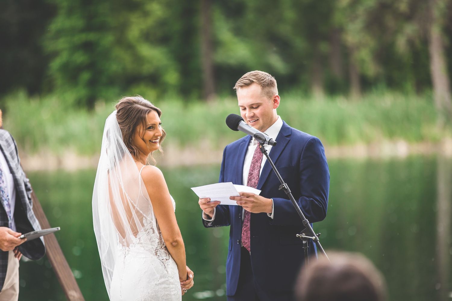 Lakeside wedding ceremony with couple exchanging vows under wooden arch.