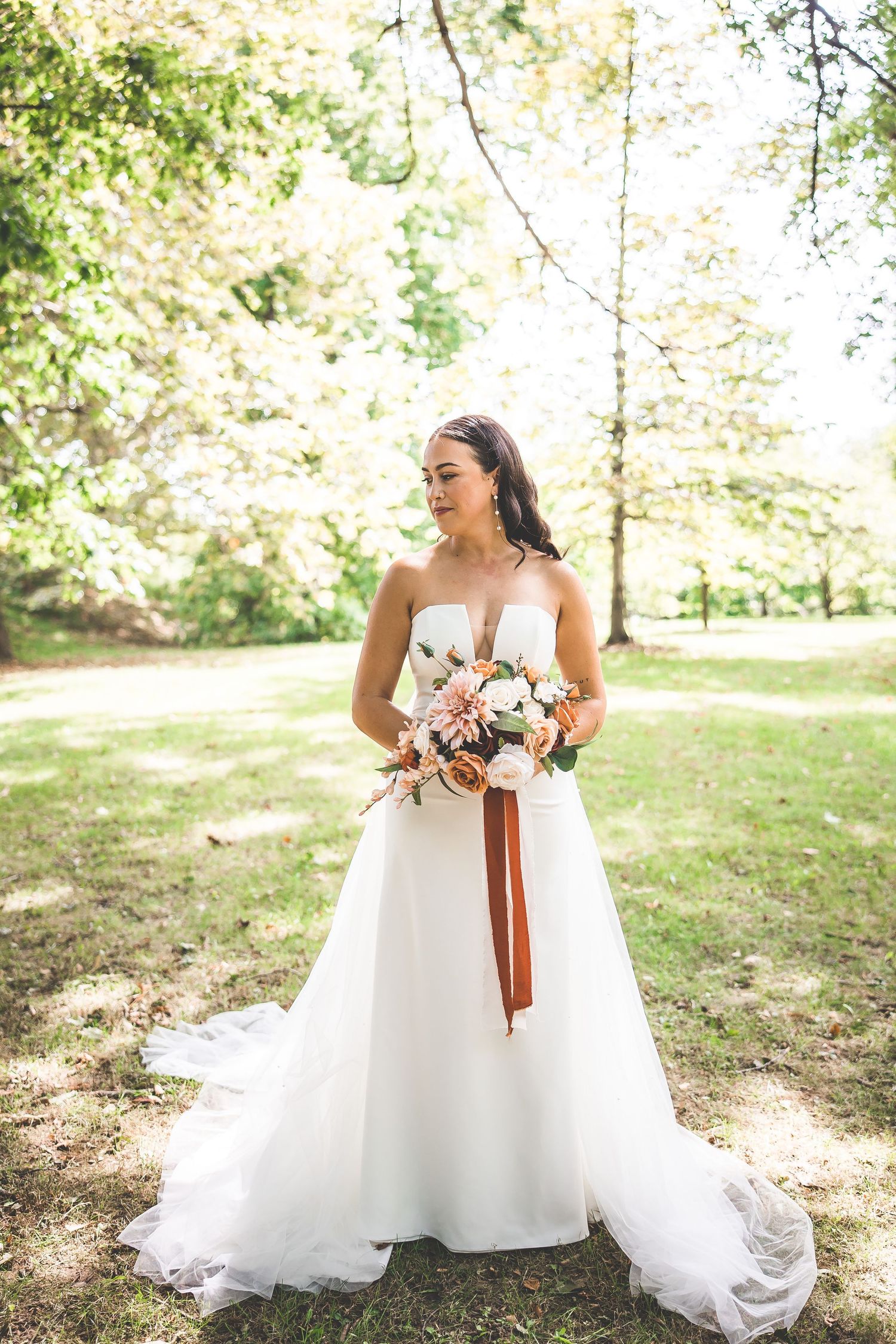 Flowing white wedding gown with delicate details photographed in a sunlit outdoor setting.