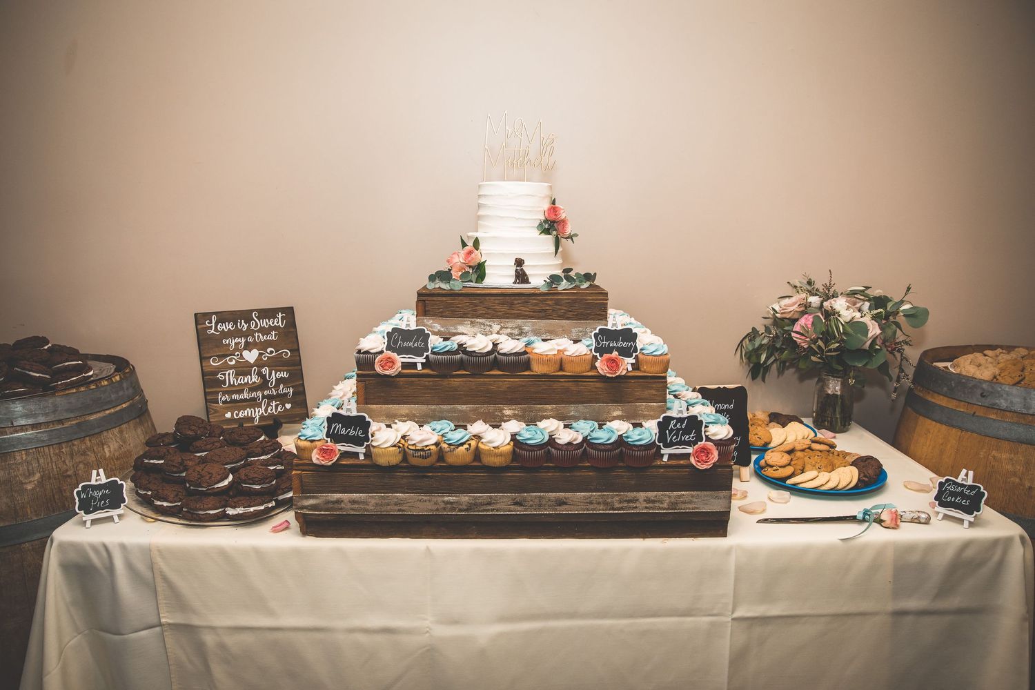 Wedding dessert table with cupcakes and cake display featuring rustic wooden decorations.