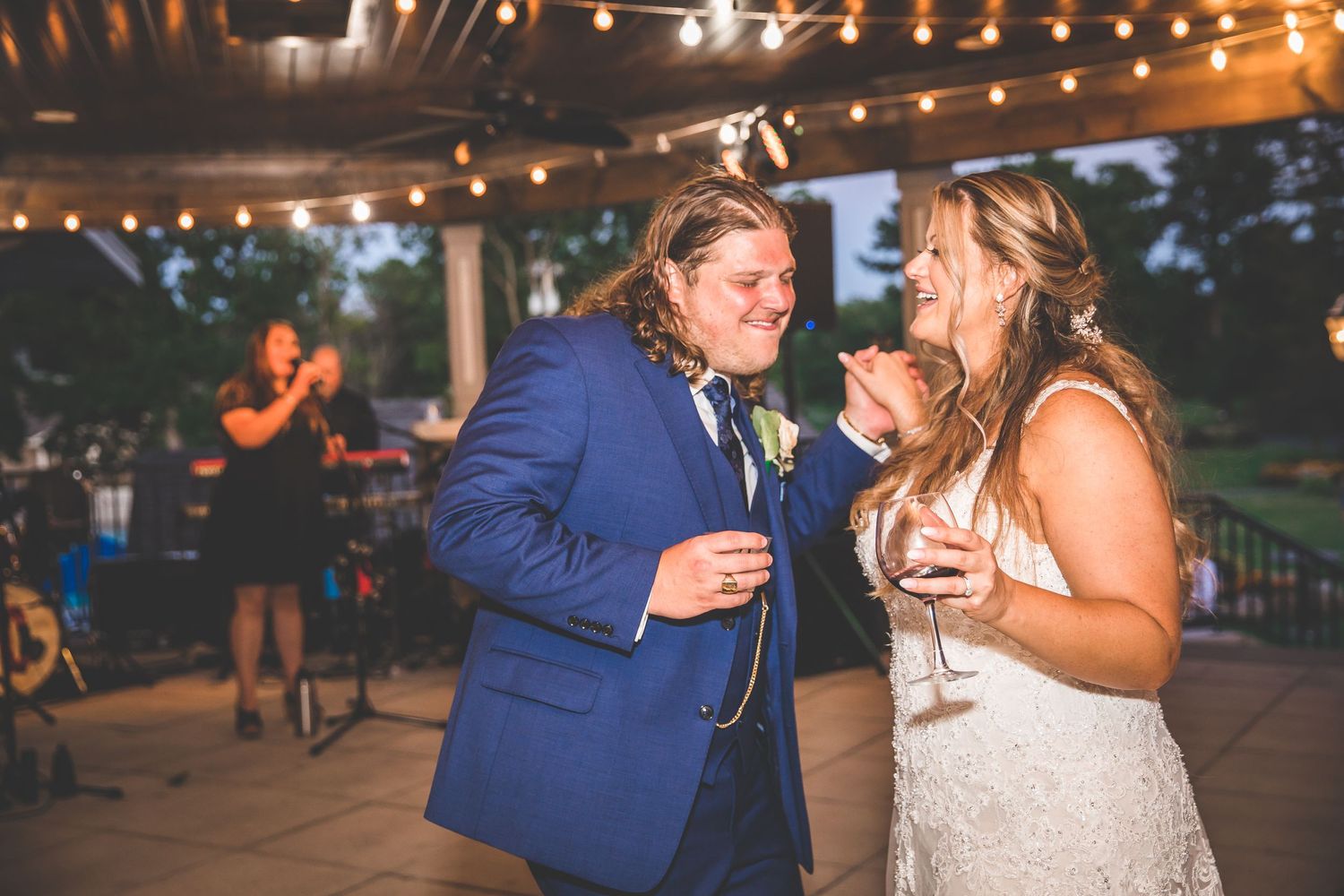 Couples dancing and celebrating under string lights at an outdoor evening reception.