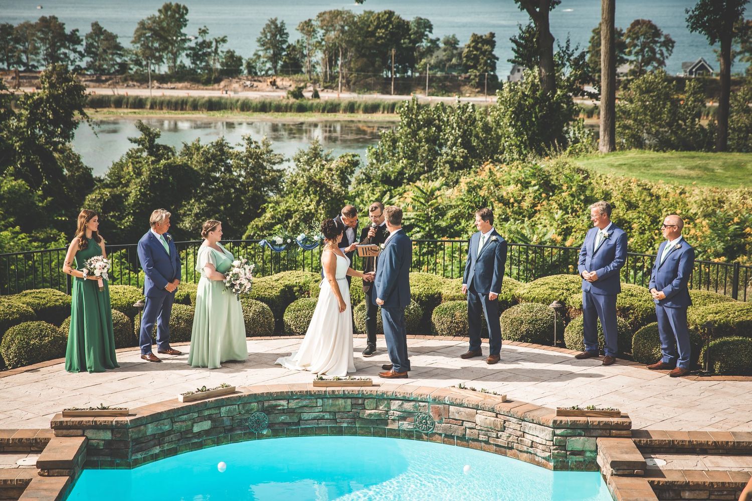 Wide view of wedding ceremony setup beside luxury pool area with guests in attendance.