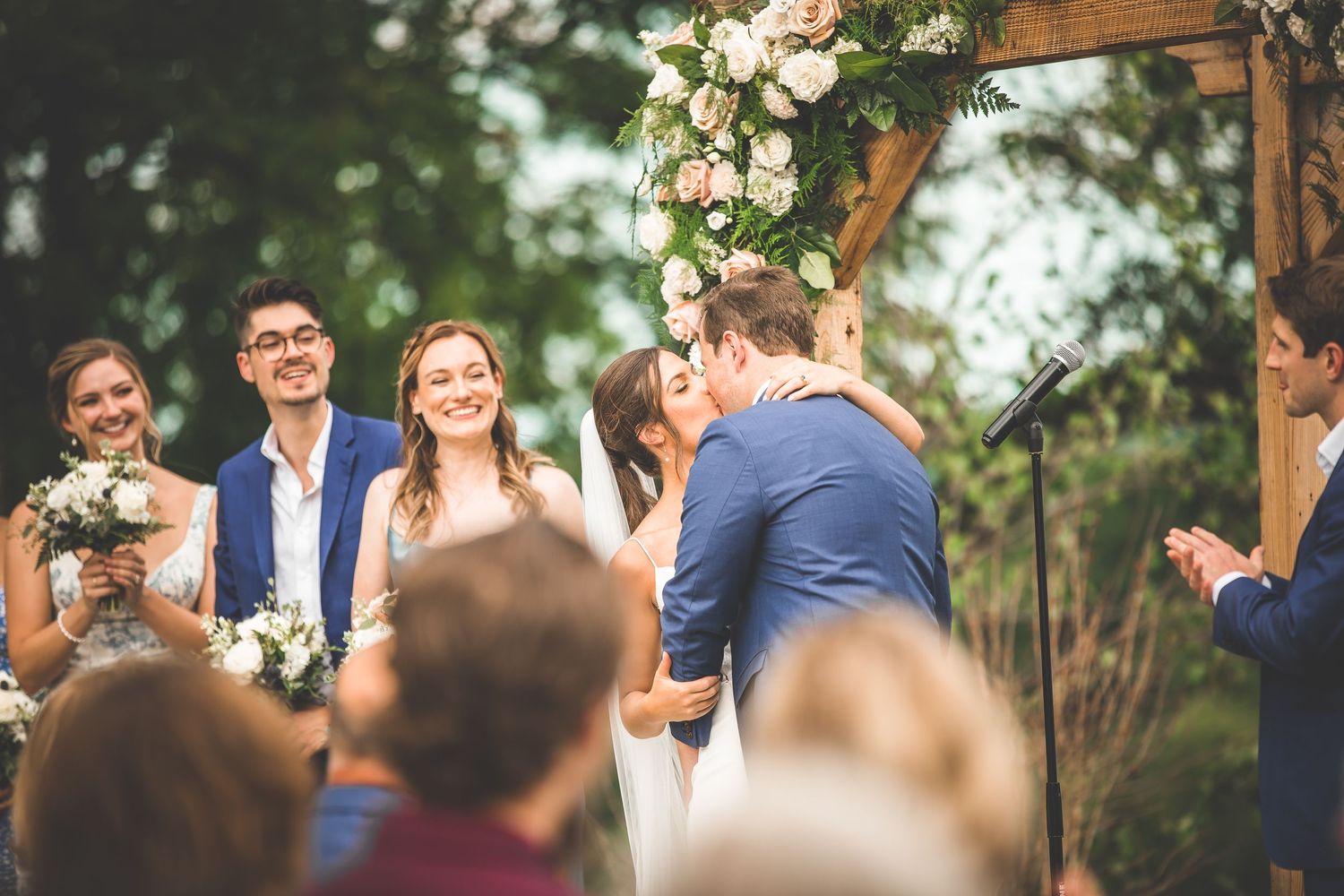 Wedding celebration with guests applauding during outdoor ceremony under decorated wooden arch.