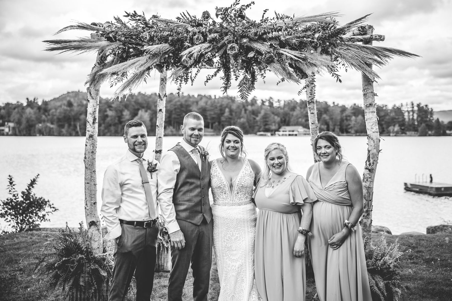 Wedding party poses together on a dock with a scenic lake and mountains in the background.