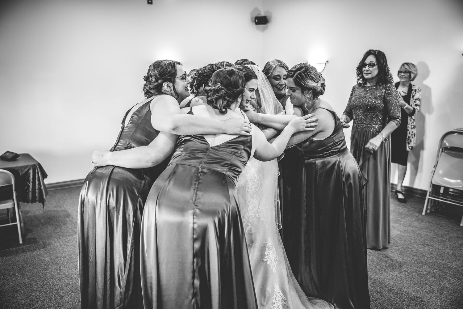 Black and white photo of bridesmaids sharing an emotional moment in a wedding venue.
