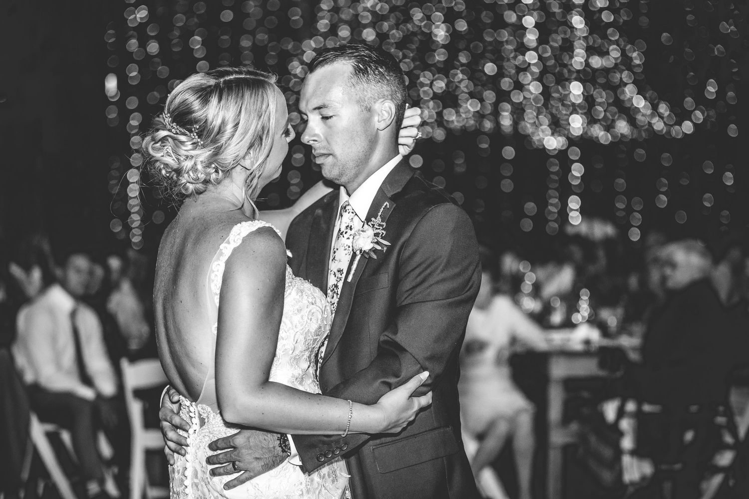 Black and white photo of a couple's romantic dance beneath sparkling lights at their wedding.