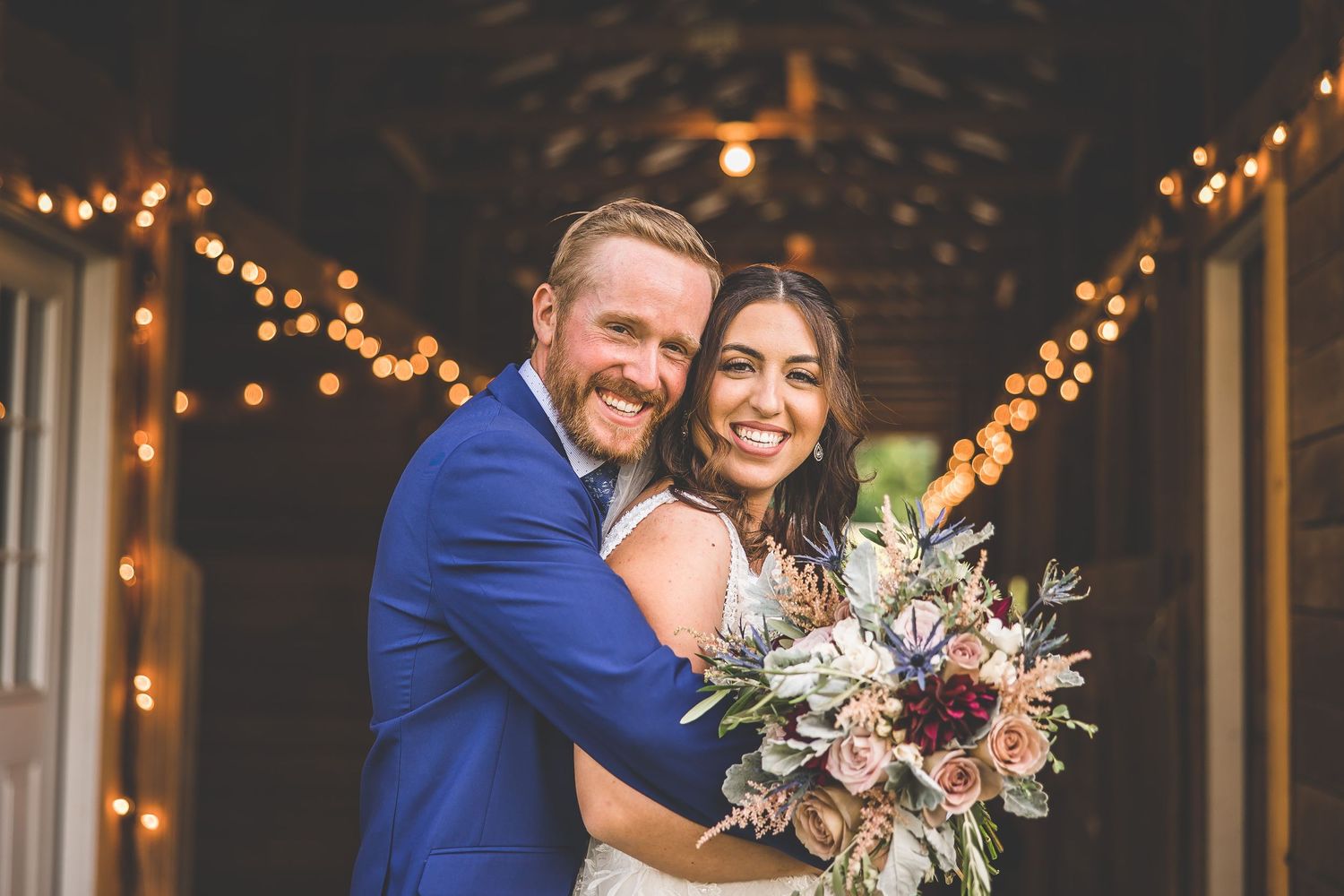 Wedding couple shares intimate moments in rustic barn venue with twinkling lights.