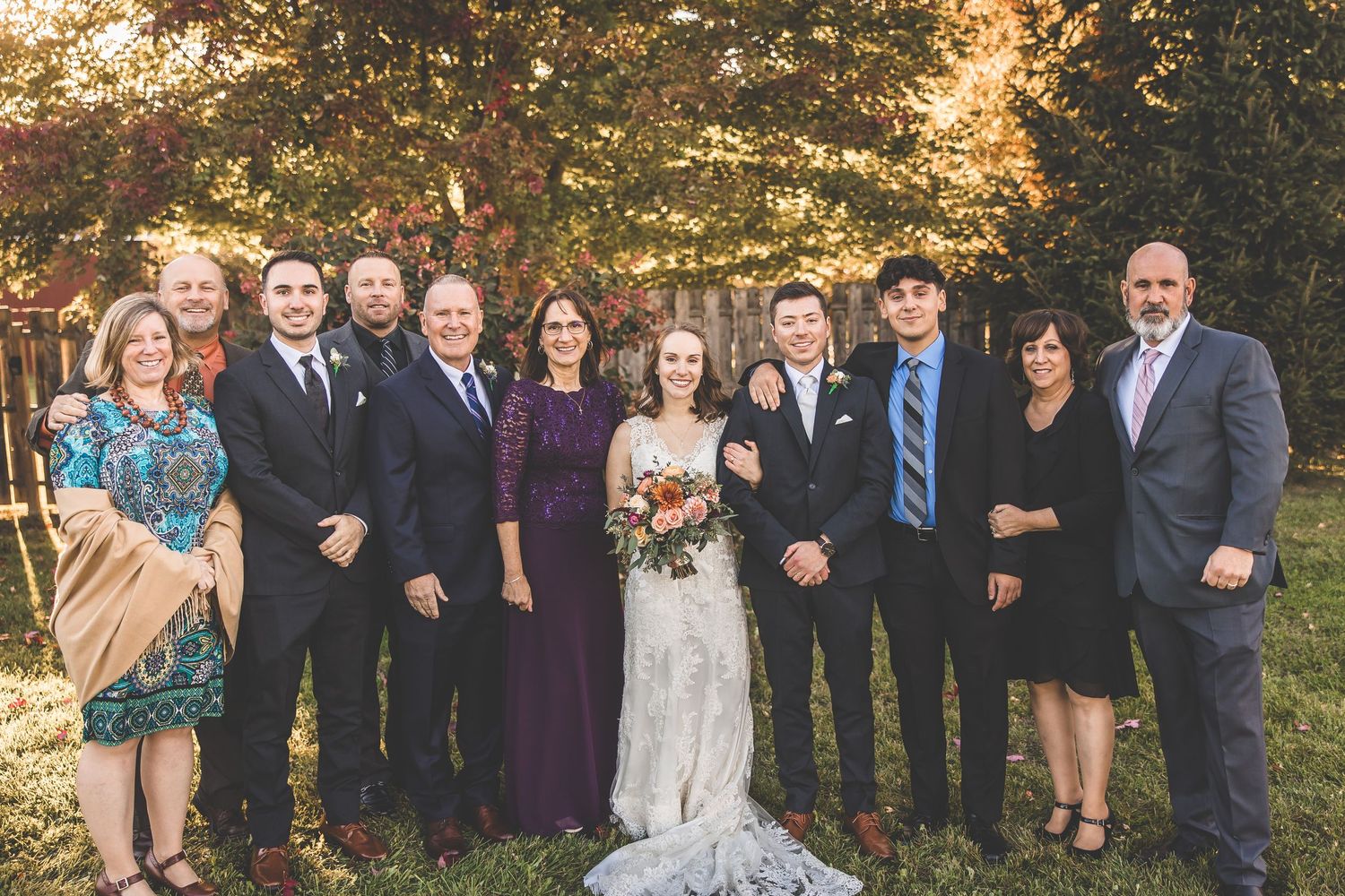 Family members gather for formal wedding portrait against autumn trees.