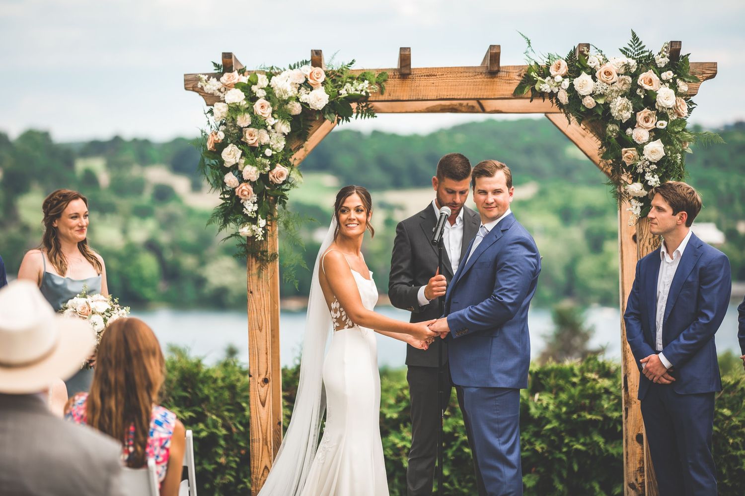 Outdoor wedding ceremony under wooden arch decorated with pink and white flowers.