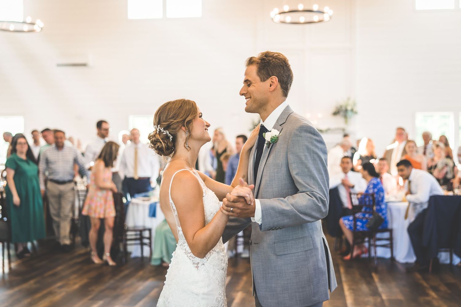 Couples share their first dance in a bright reception hall with modern lighting fixtures.