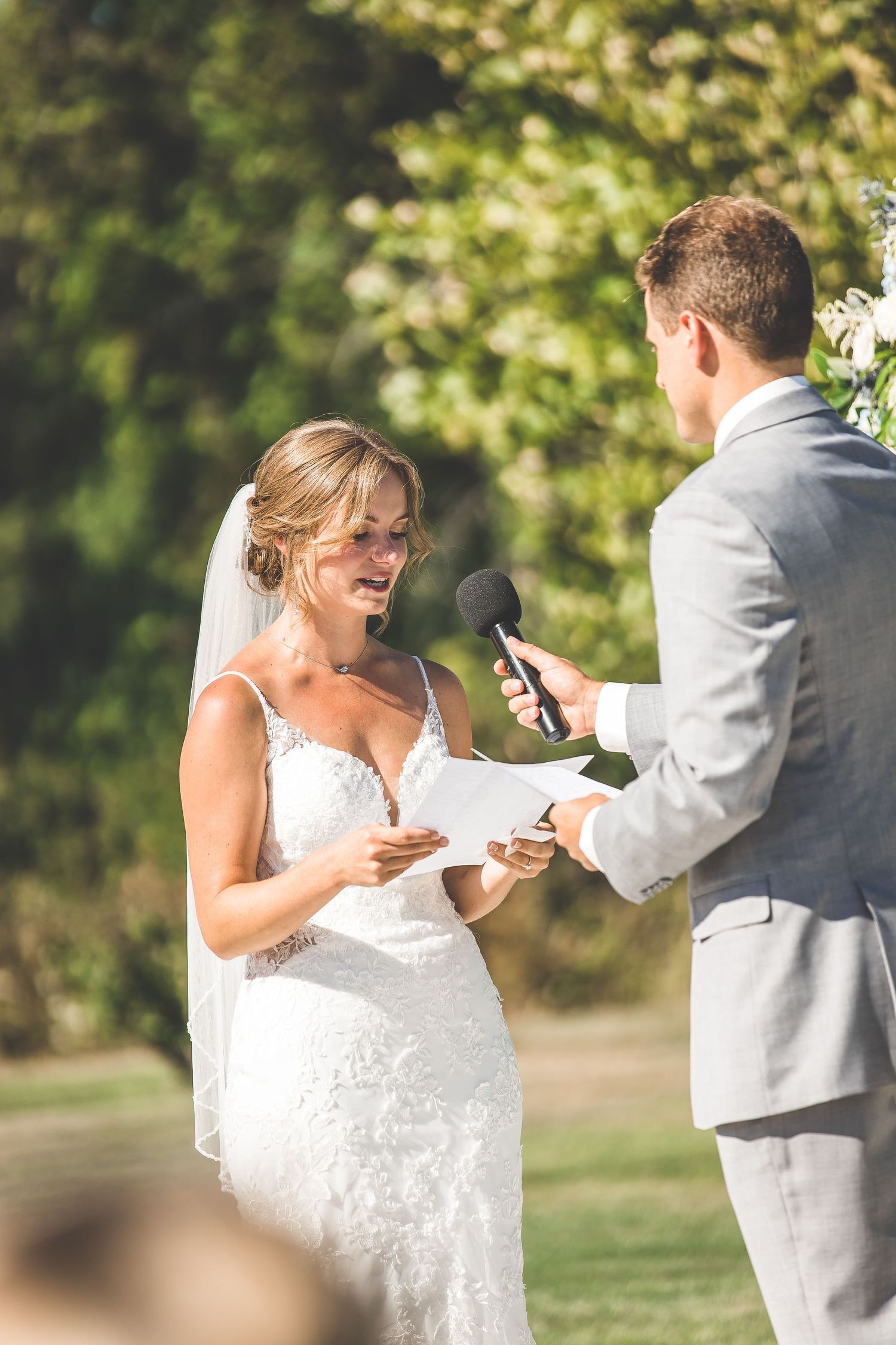 Wedding couple exchanging vows under a wooden arch with floral decorations in an outdoor garden setting.