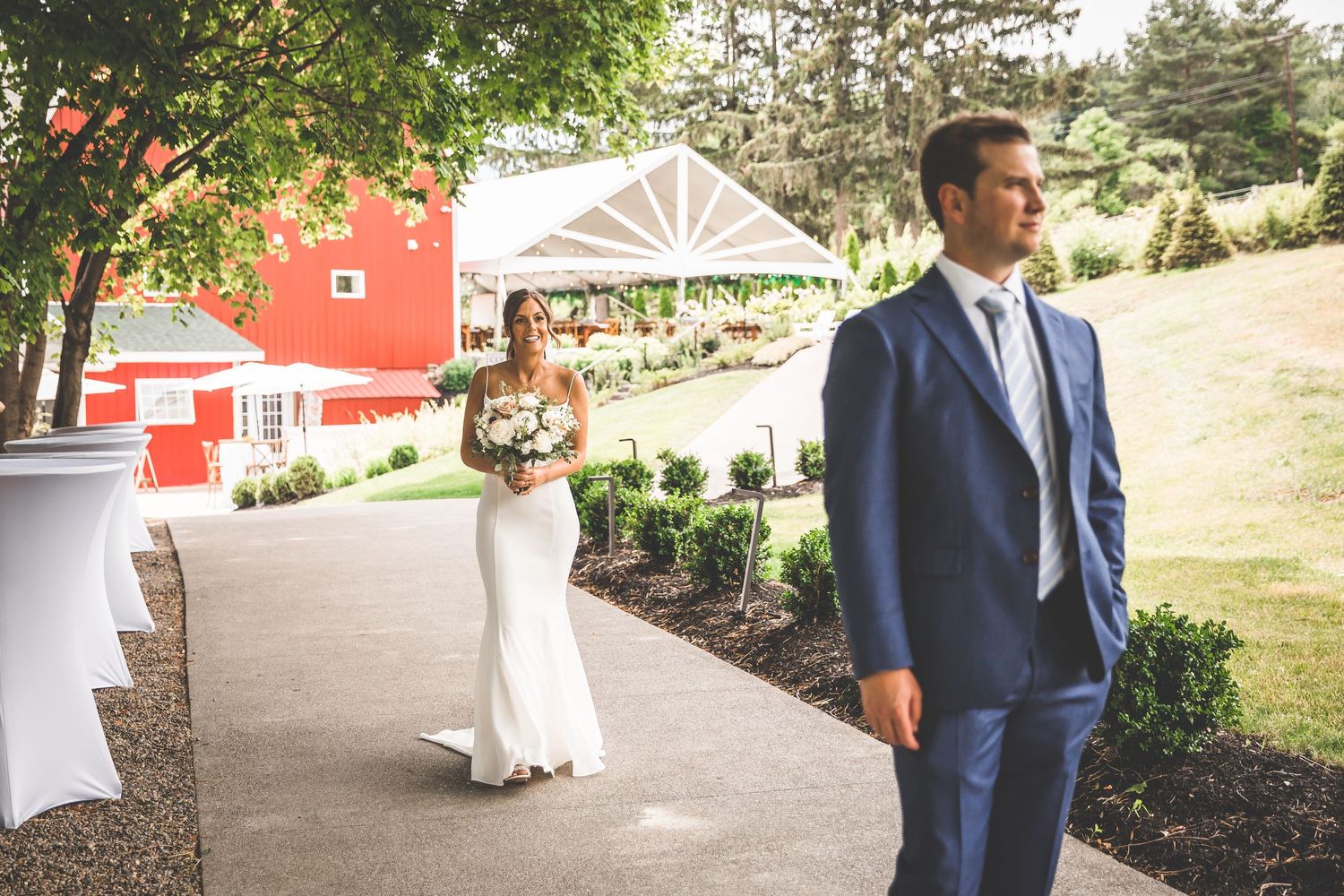 Outdoor wedding venue with red barn and landscaped path on sunny day.