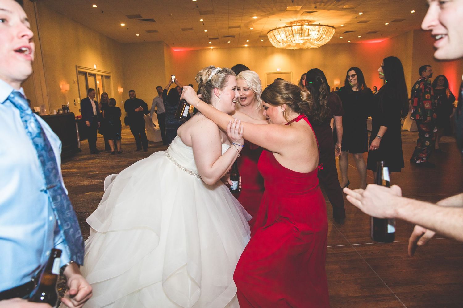 Wedding reception guests dancing and celebrating on a dance floor illuminated by warm lighting.