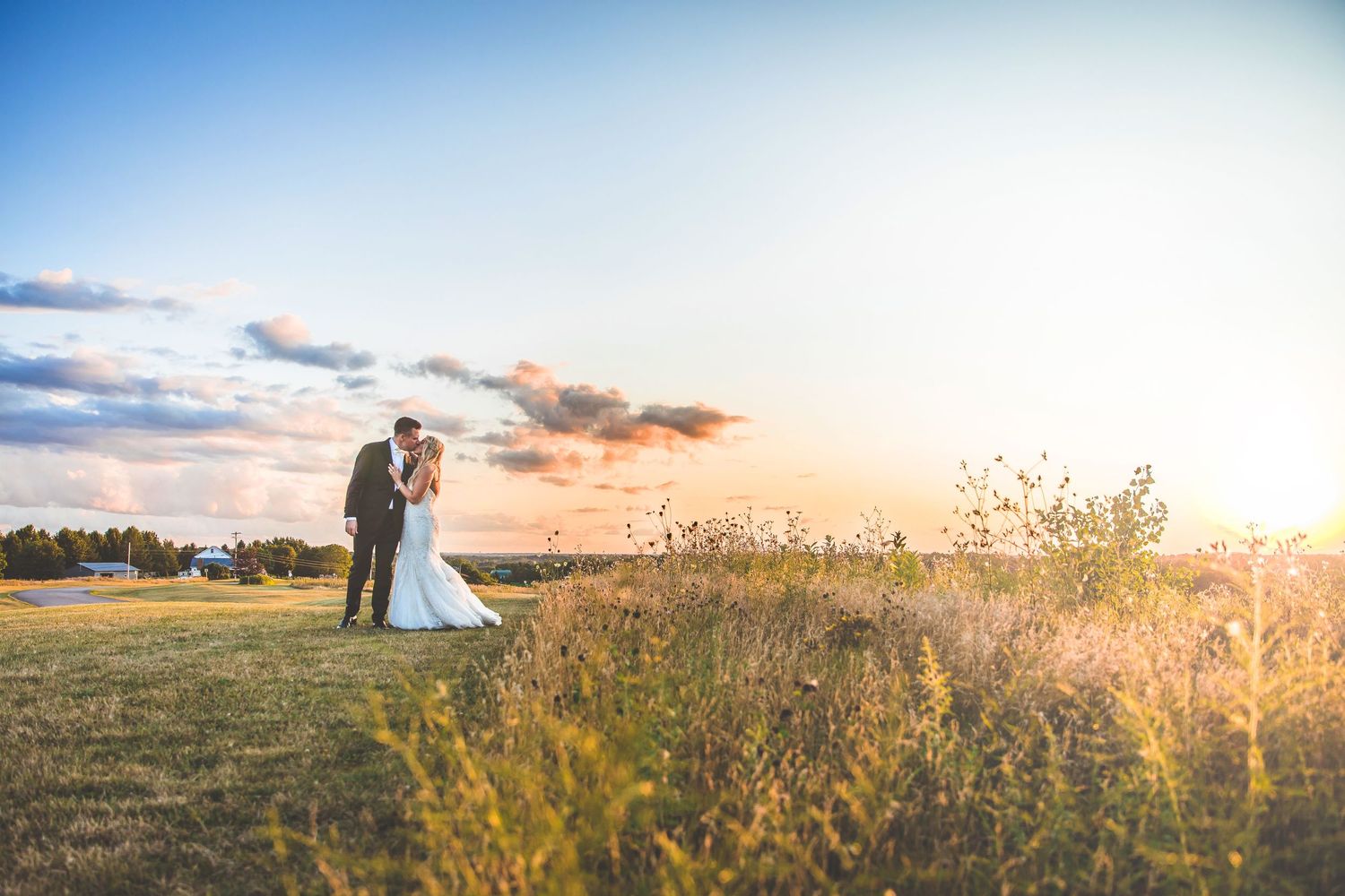 Wedding couple walks through a golden field at sunset with dramatic sky.