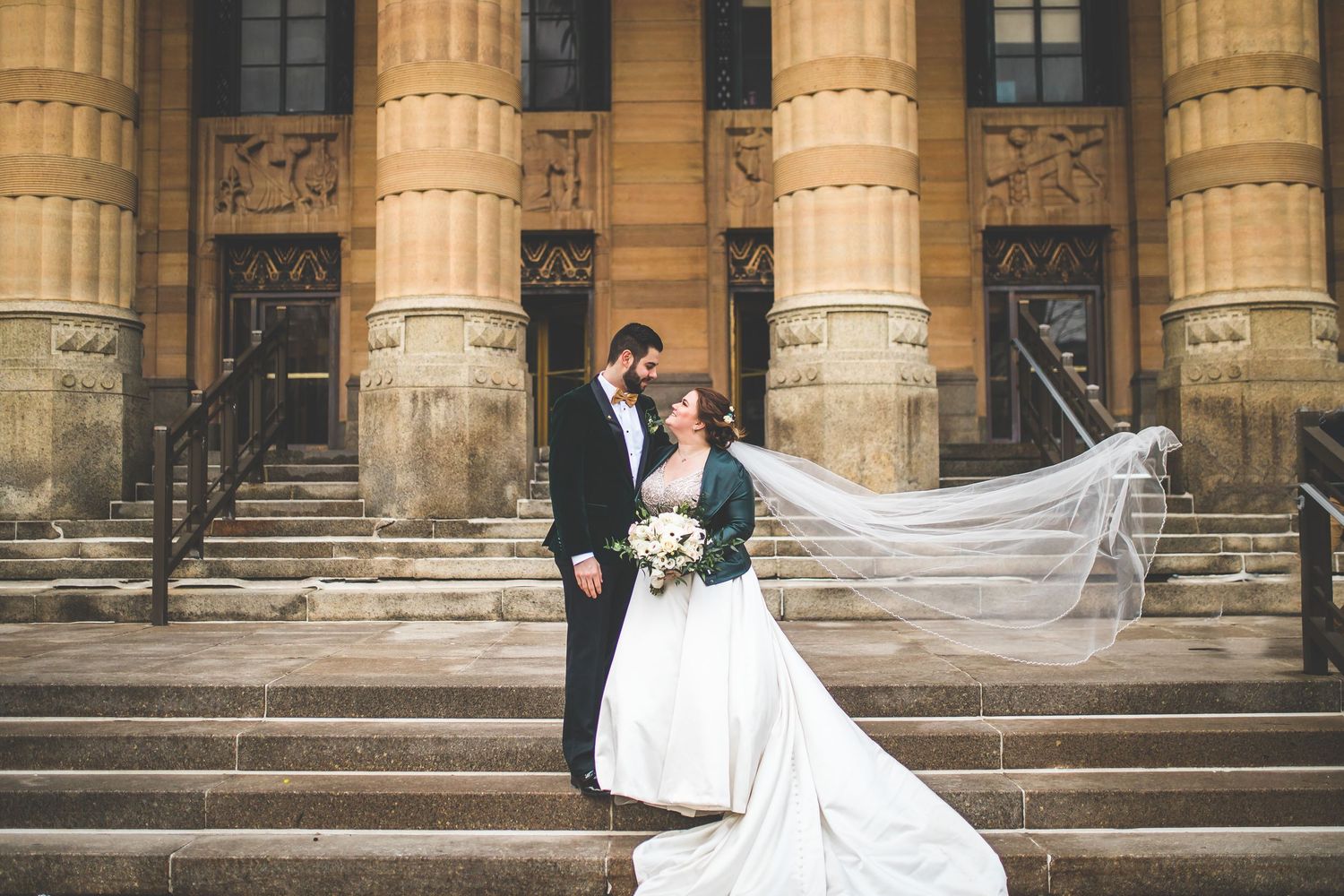 Elegant wedding portraits with flowing veil against historic building facade.