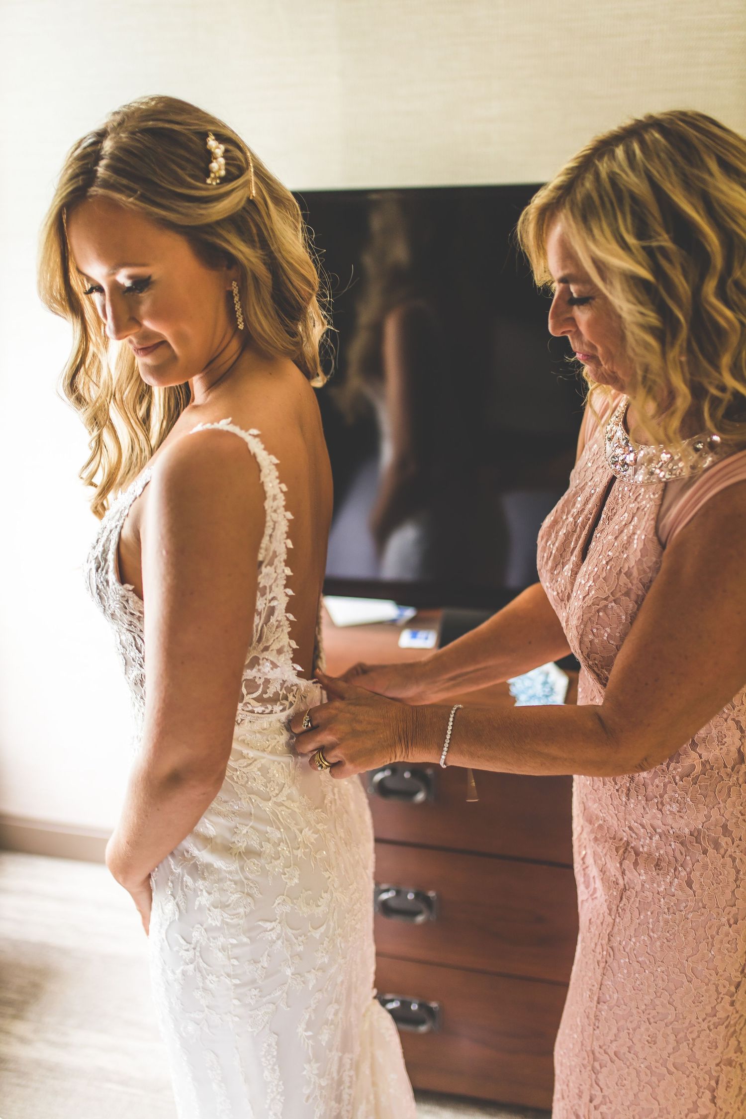 Bride in white lace gown getting final adjustments from wedding party.