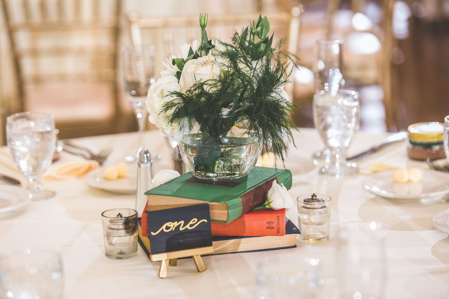 Wedding reception table setting with green centerpiece and vintage book decor.