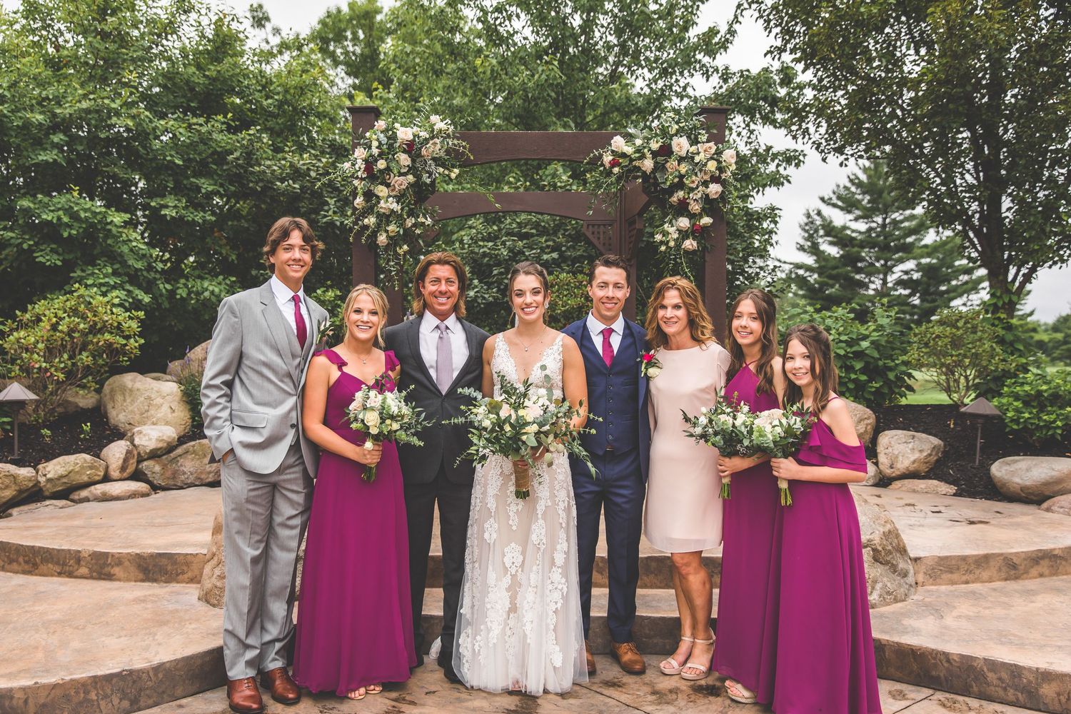 Large group wedding photo with bridal party in burgundy and grey attire.