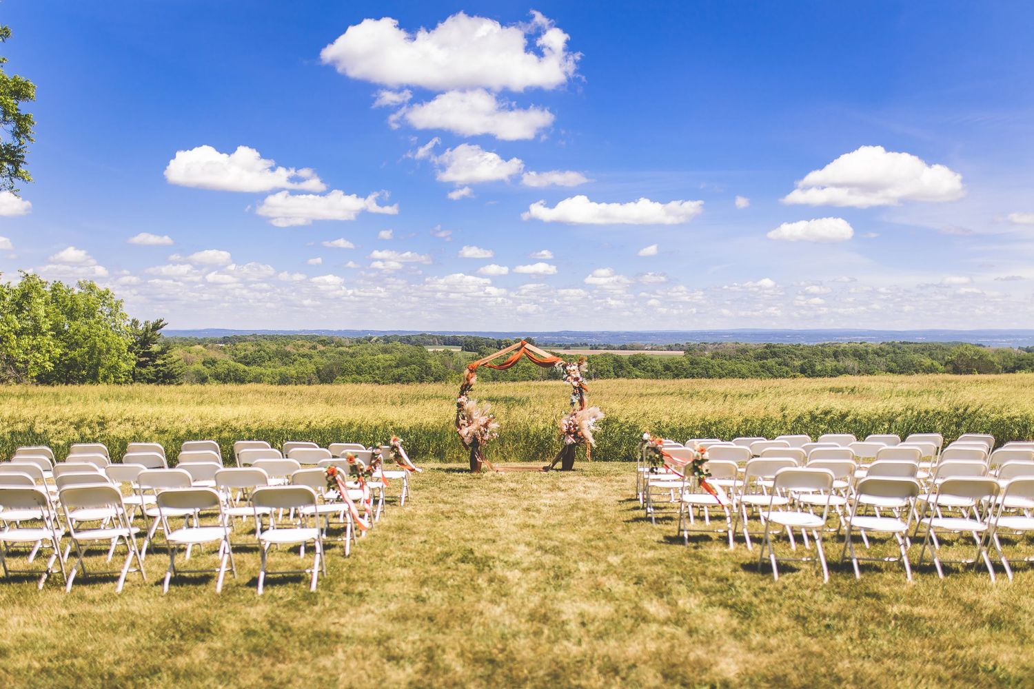 White chairs set up for an outdoor wedding ceremony in a scenic field under blue skies.