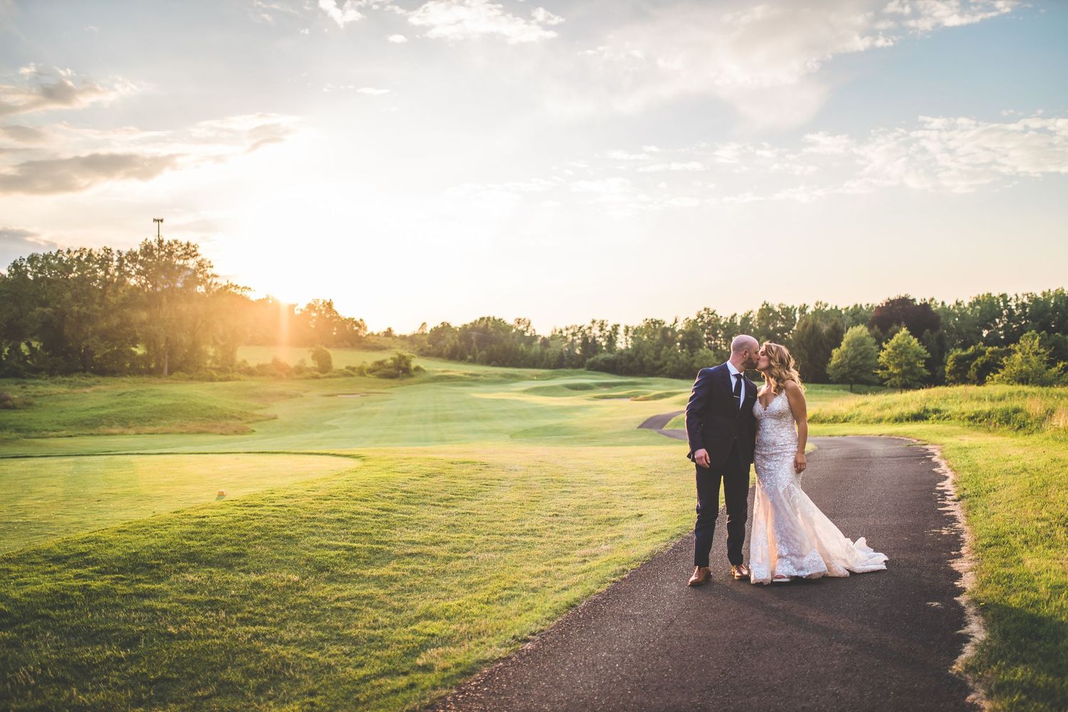 Golden sunset illuminates a wedding couple walking along a path at a golf course.