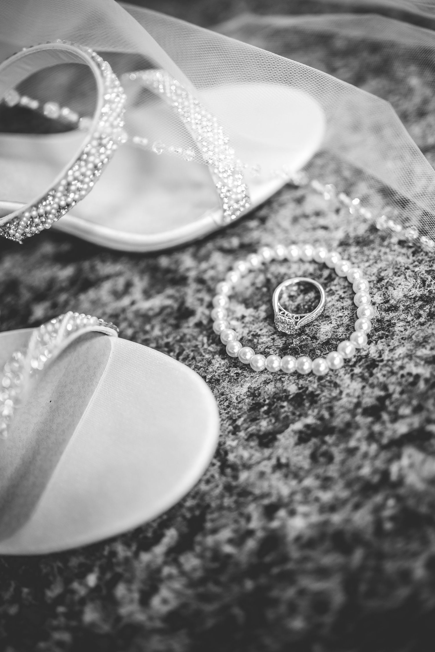 Wedding rings and bridal shoes with crystal details on textured stone surface.