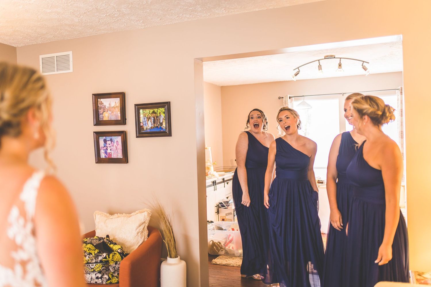 Bridesmaids in navy blue dresses help with wedding preparations in a sunlit room.