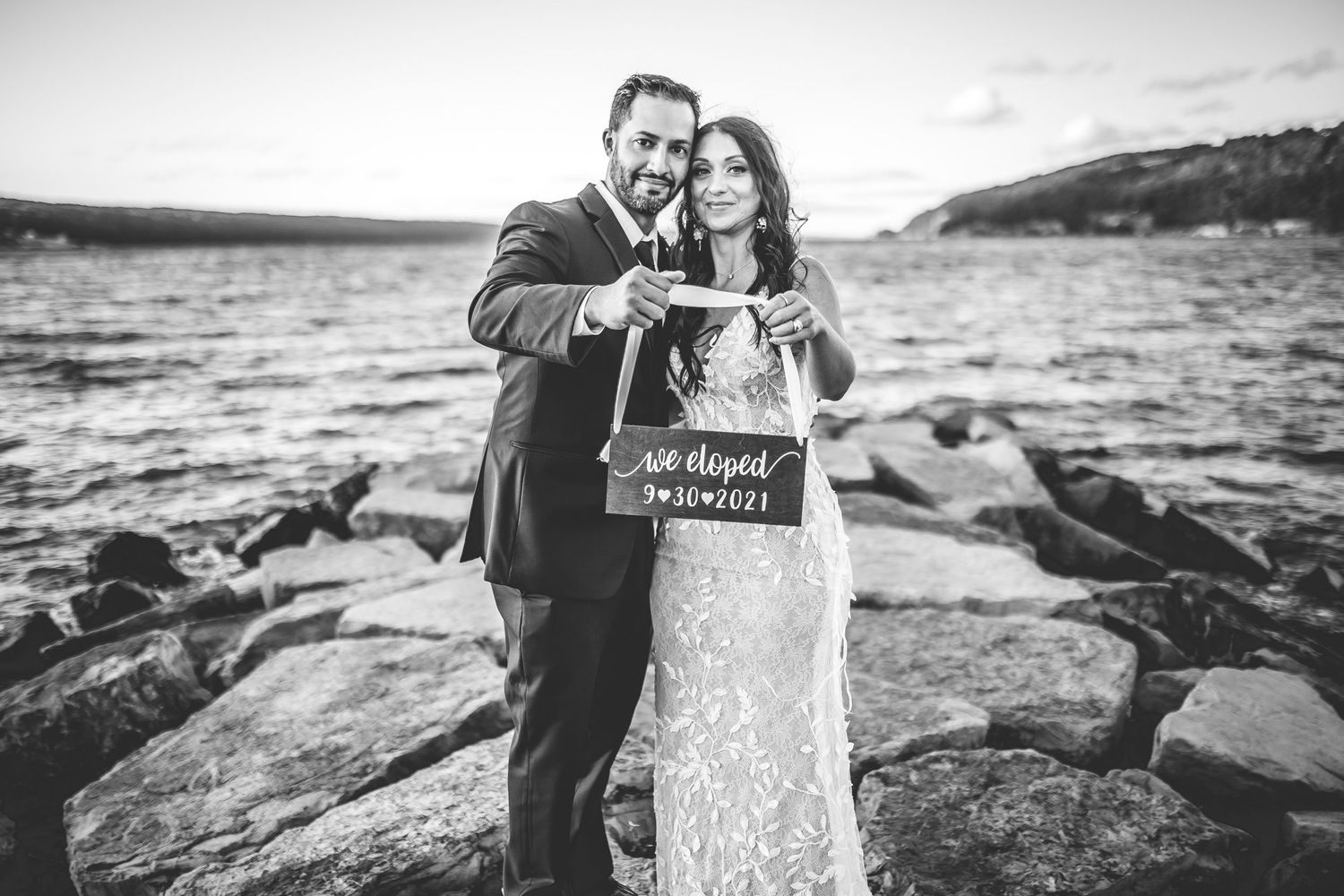 Wedding couple embraces on rocky coastal shoreline during golden hour.