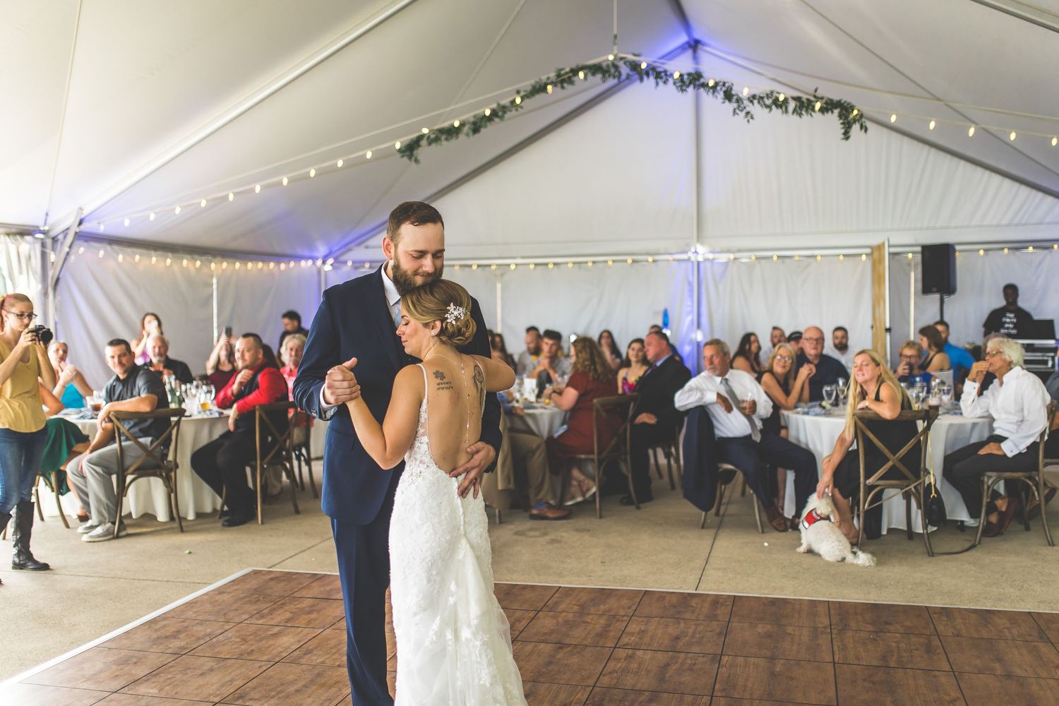 Couple dancing at their wedding reception in a tent venue with string lights and wooden flooring.
