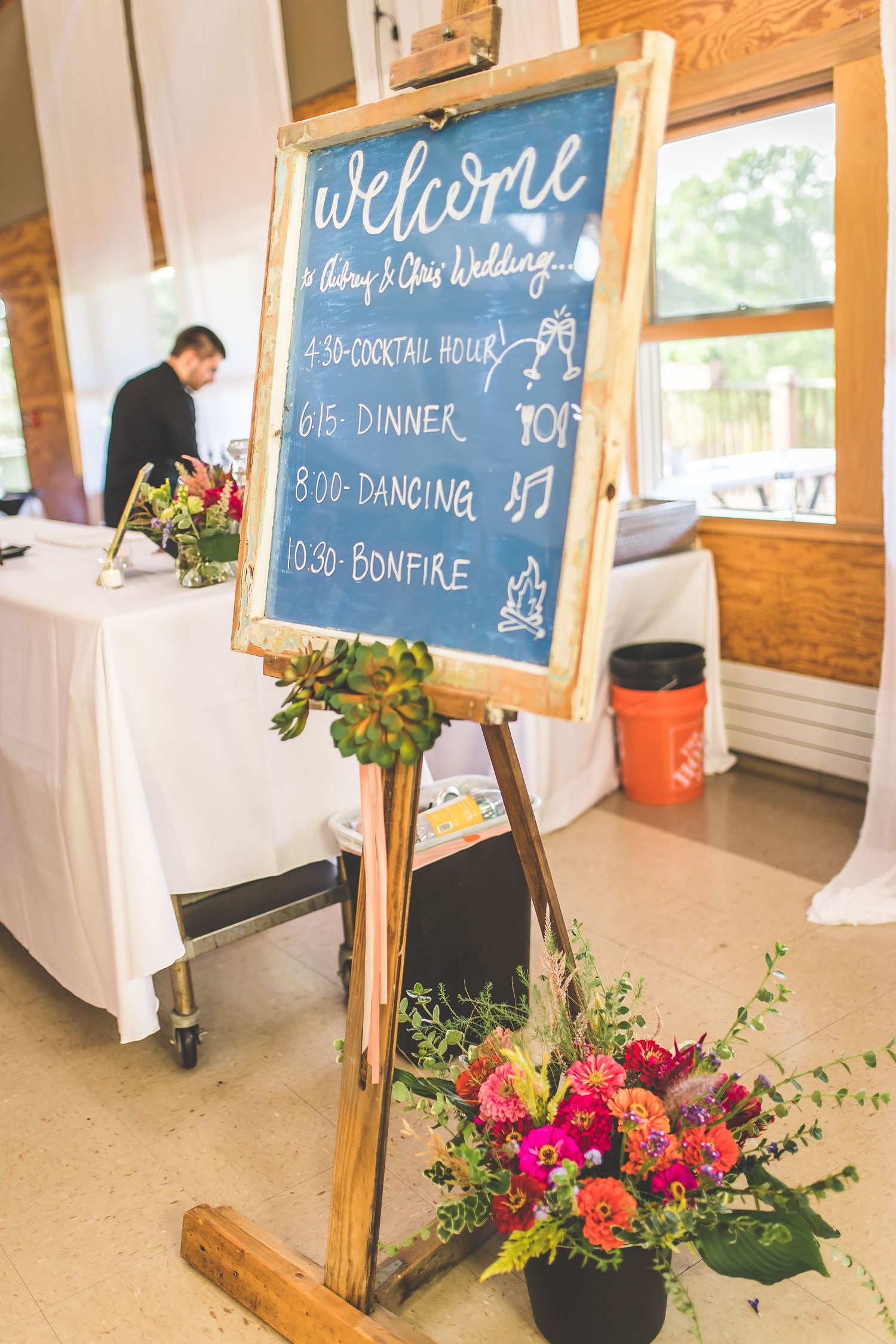 A wedding welcome sign with schedule details decorated with bright floral arrangements.