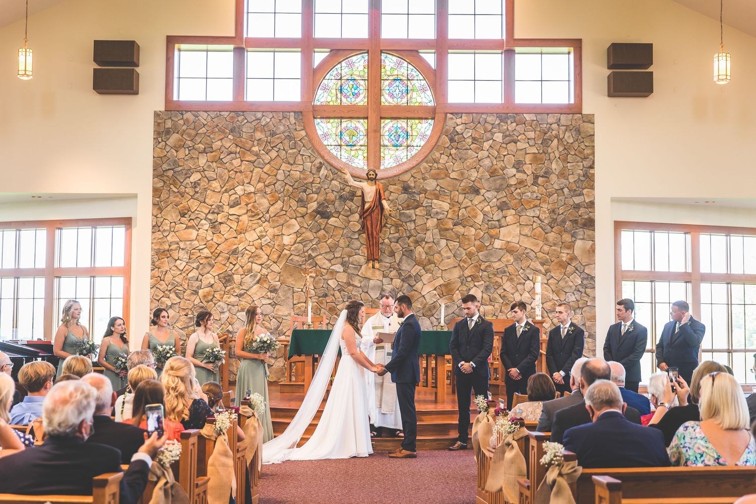 A panoramic view of a church wedding ceremony with stone walls and large windows.