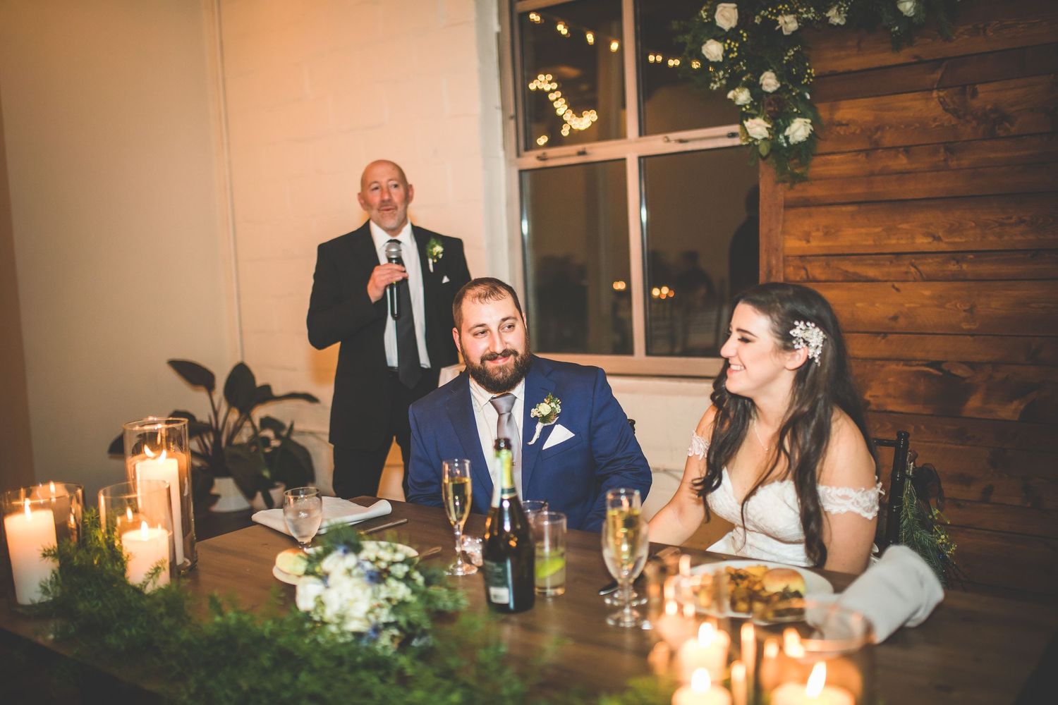 Wedding reception dinner setup with candlelit tables and rustic wood paneled walls.