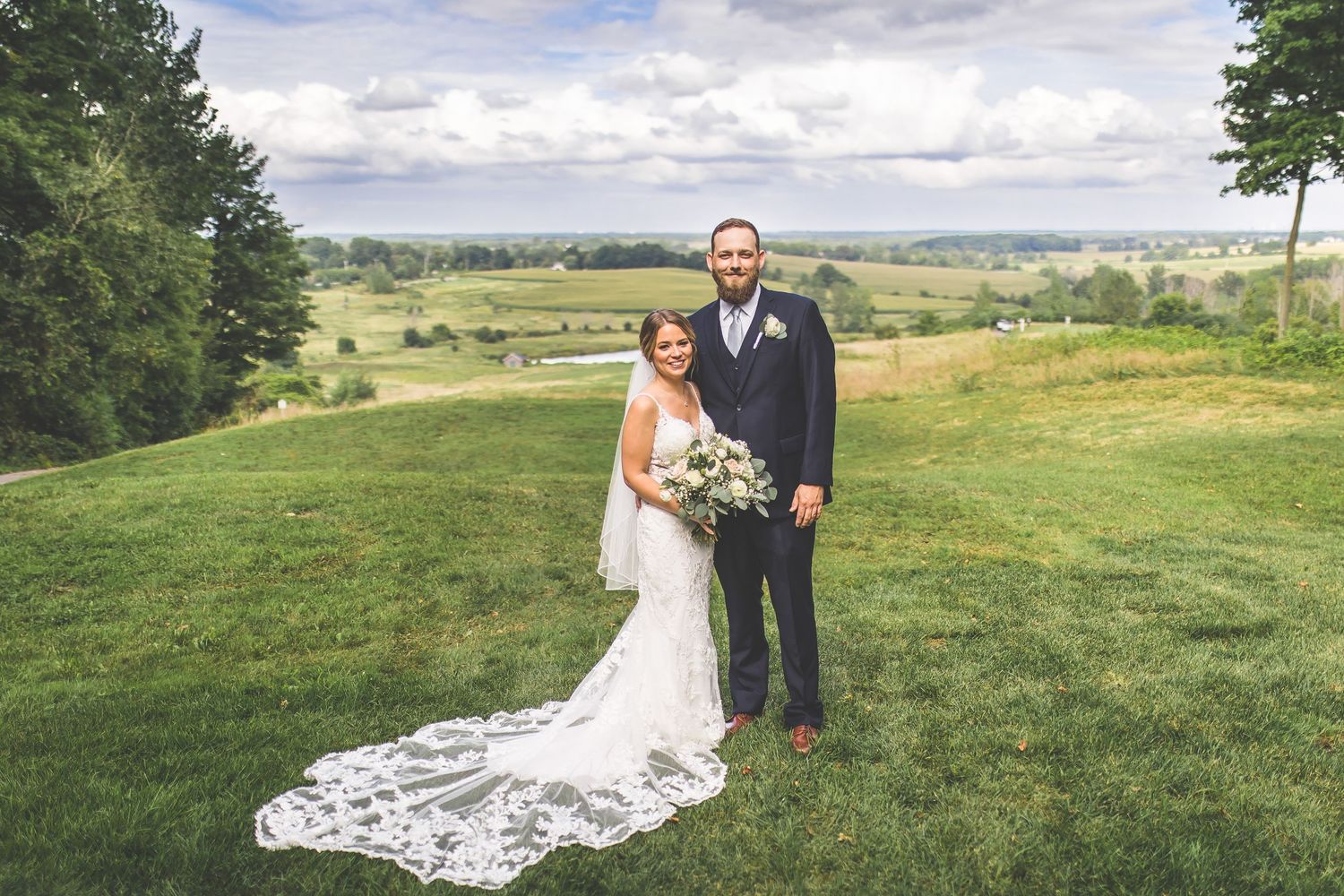 Elegant outdoor wedding ceremony setup on rolling hills with long white train detail.