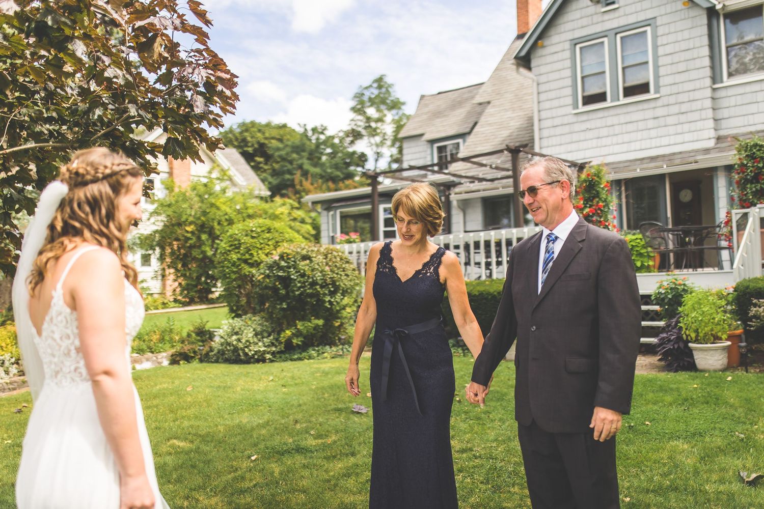 Wedding party poses together outdoors on a sunny day with green lawn and houses in background.