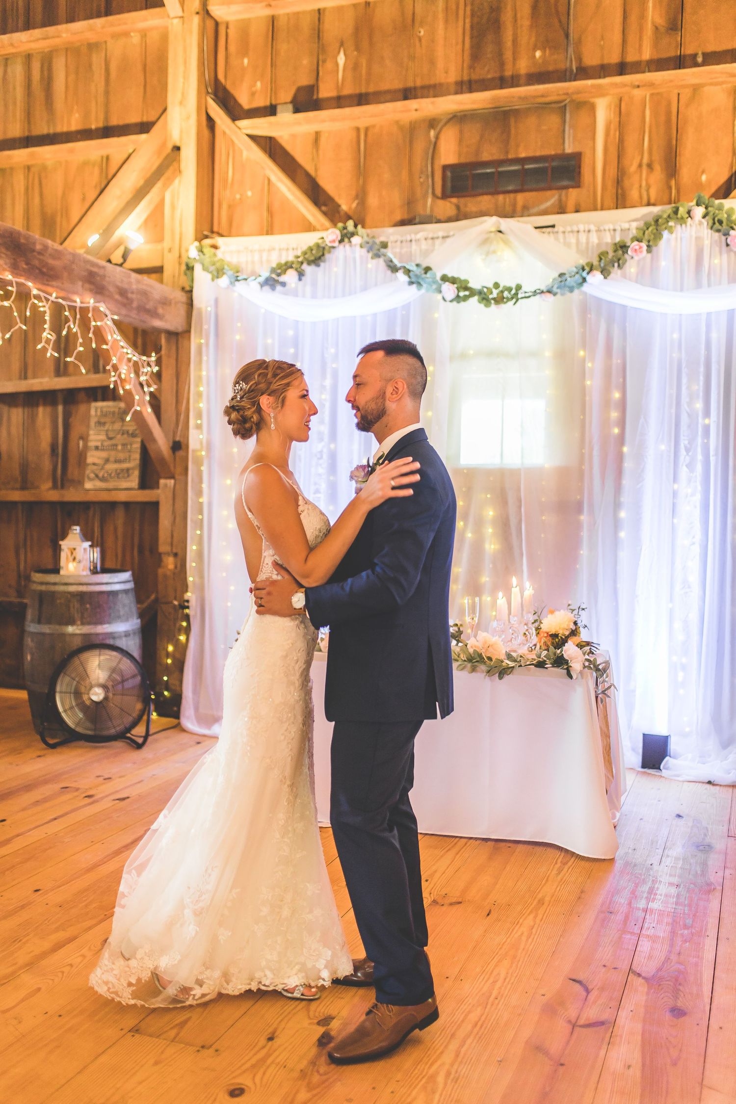 First dance in a rustic barn venue with white fabric backdrop and string lights.