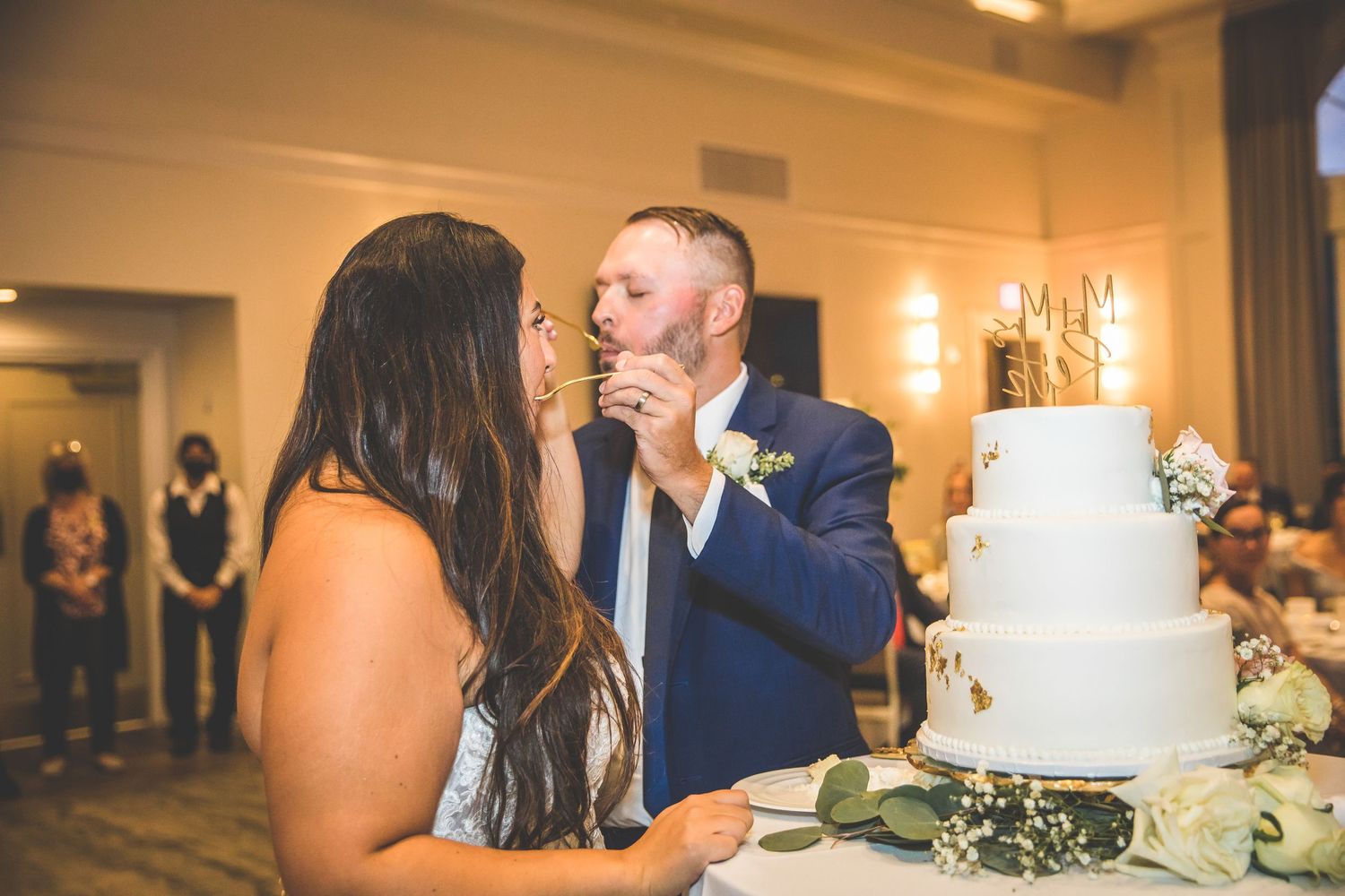 Wedding reception guests enjoying cake cutting ceremony in an elegant ballroom venue.