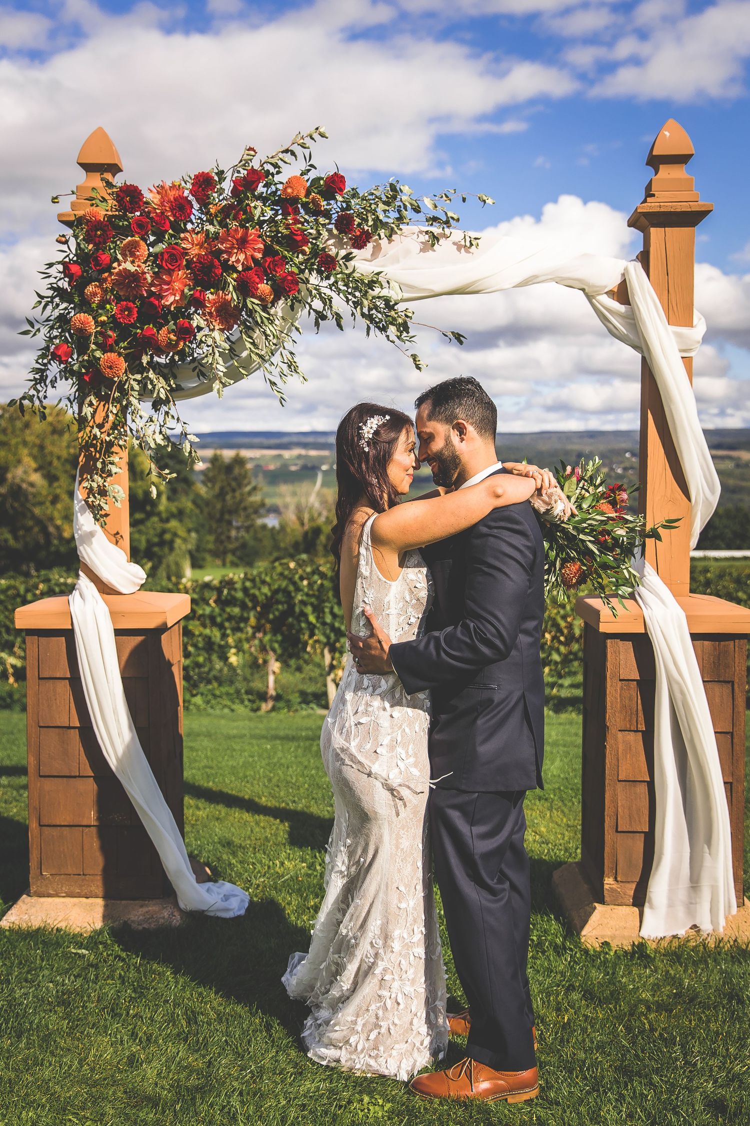 Wedding couple sharing a romantic moment under a decorated arch in a vineyard setting.