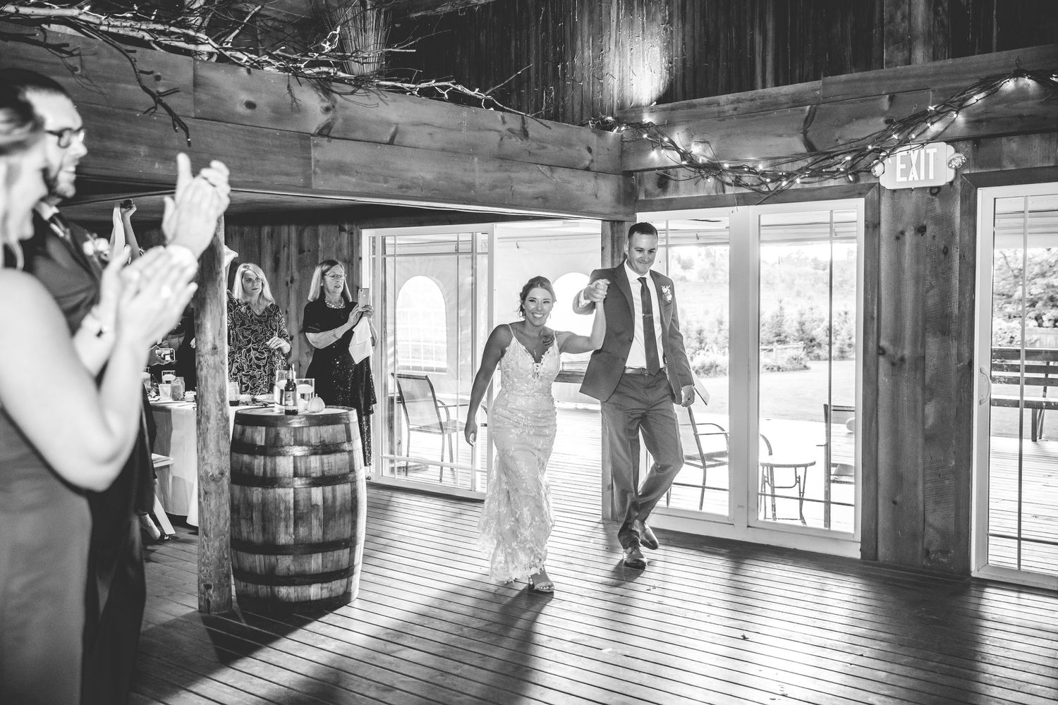 Wedding guests dancing in rustic barn venue with natural light streaming through windows.