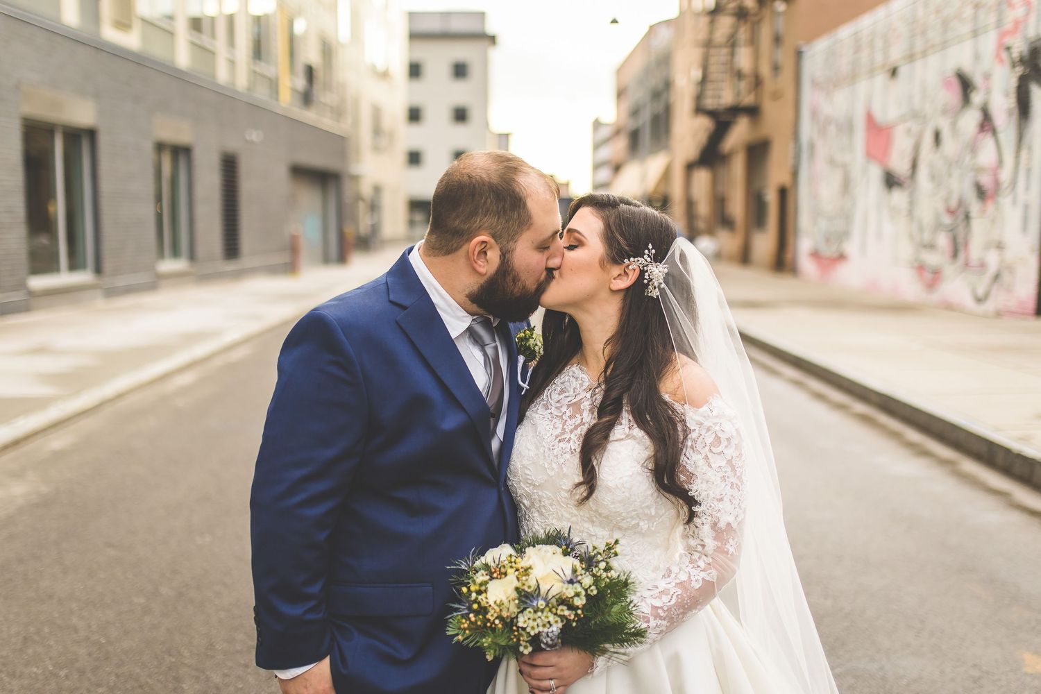 Wedding couple shares intimate moments on city street with buildings in background.