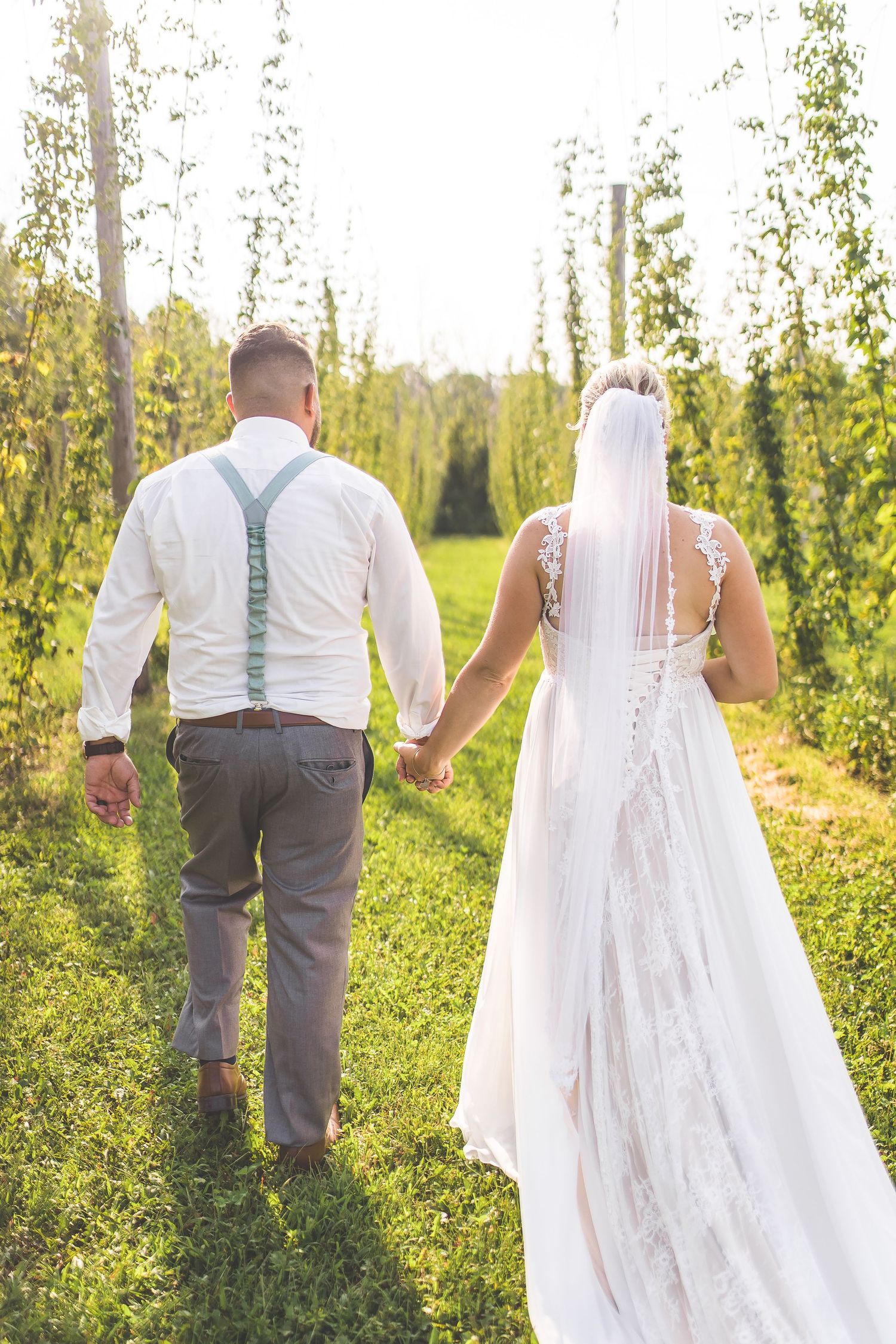 Wedding couple walks hand in hand through a lush garden path at sunset.