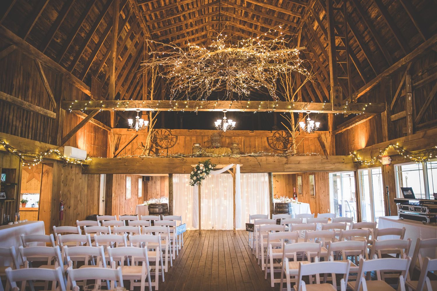Rustic barn wedding venue interior set up with rows of white chairs and wooden beams.