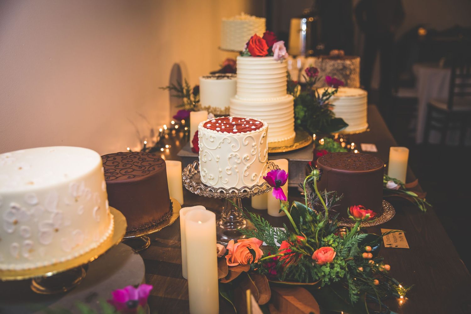Elegant wedding cake display with vibrant red and pink floral decorations against a warm-lit background.