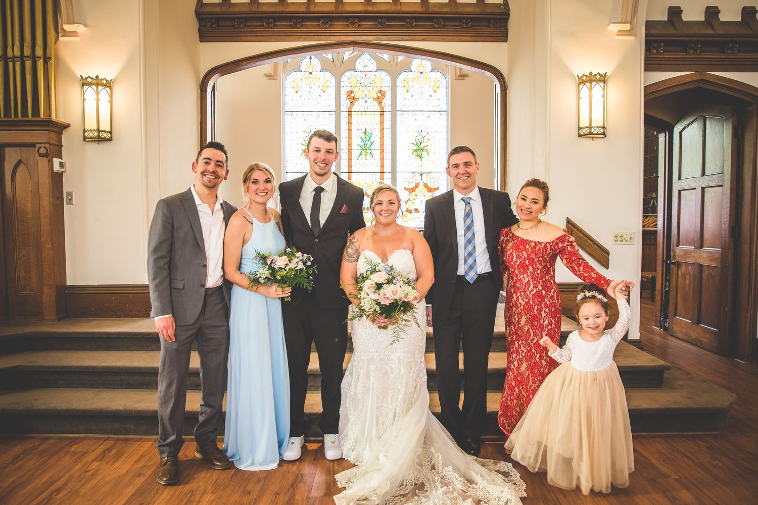 Wedding party poses together inside a beautiful church with stained glass windows and wooden details.