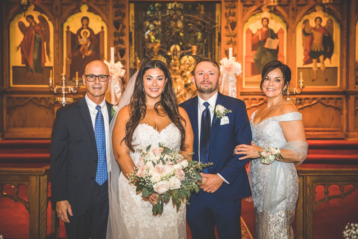Wedding party poses in front of ornate church altar with golden details and religious artwork.