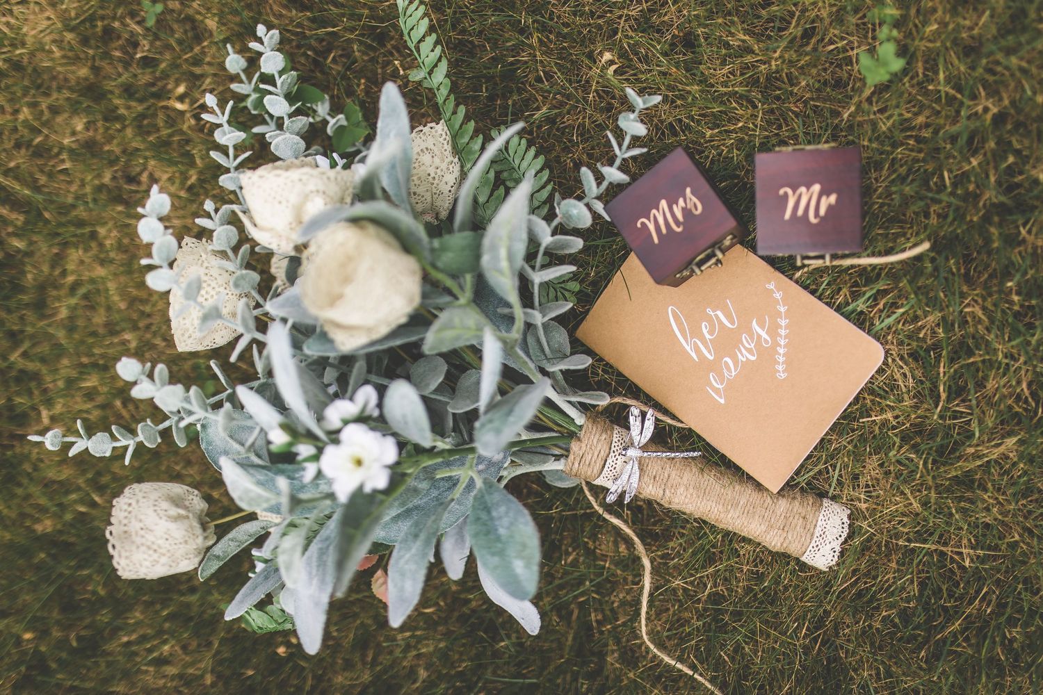 Wedding floral arrangements with eucalyptus leaves and decorative signs laid on grass.