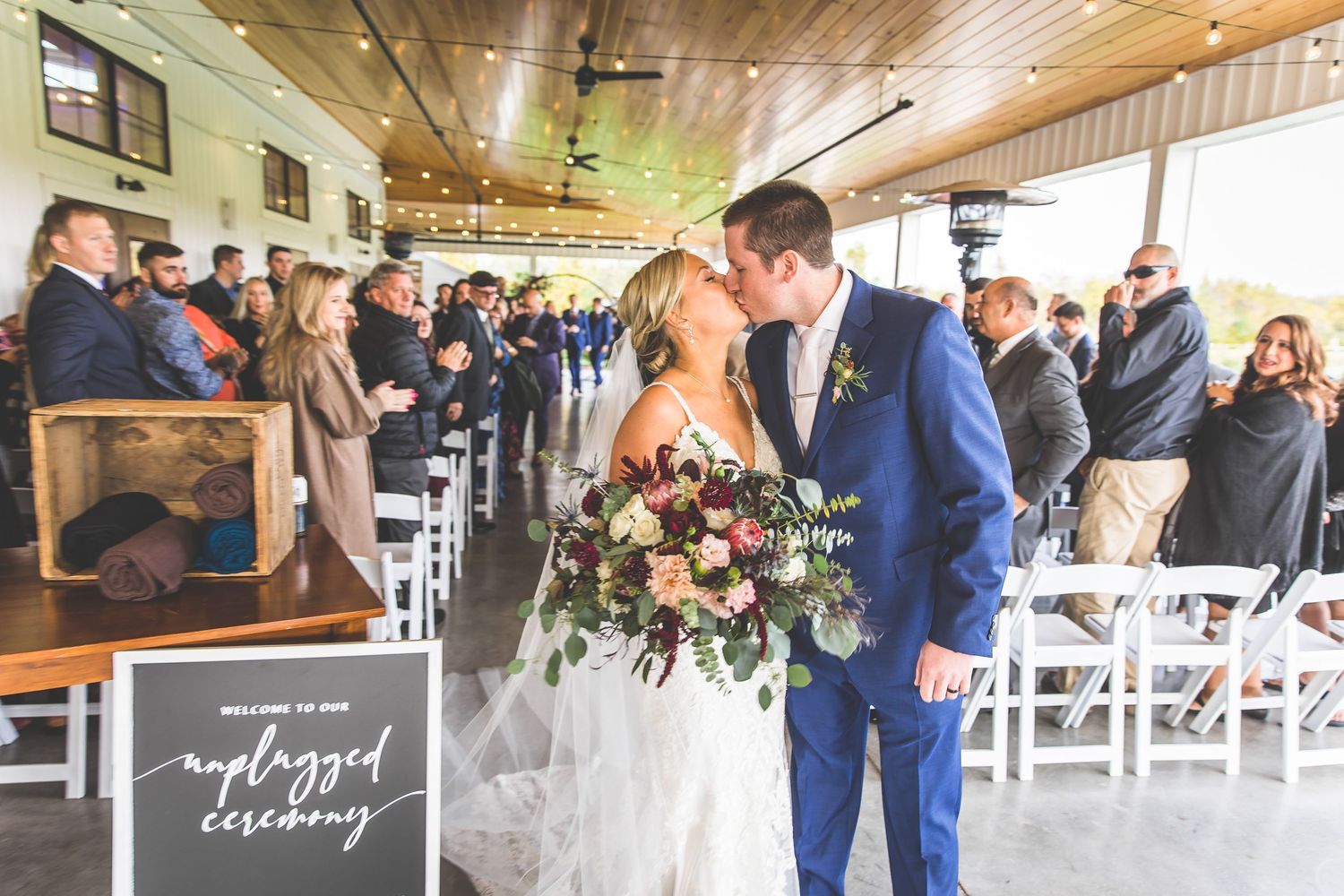 Wedding exit with guests lining aisle in modern venue with wooden ceiling and white chairs.