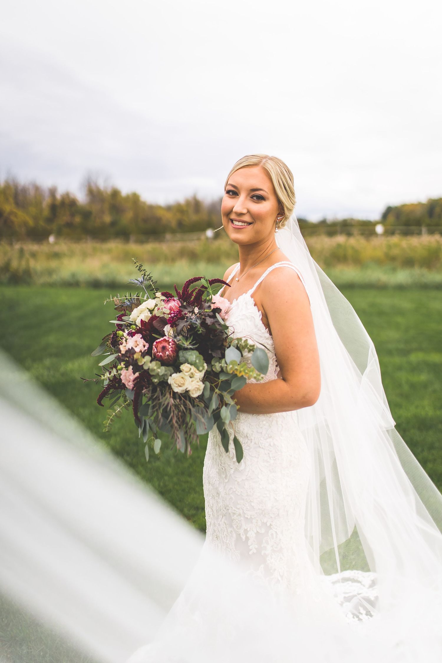 A bride holds a stunning bouquet of pink and white flowers against her lace gown.