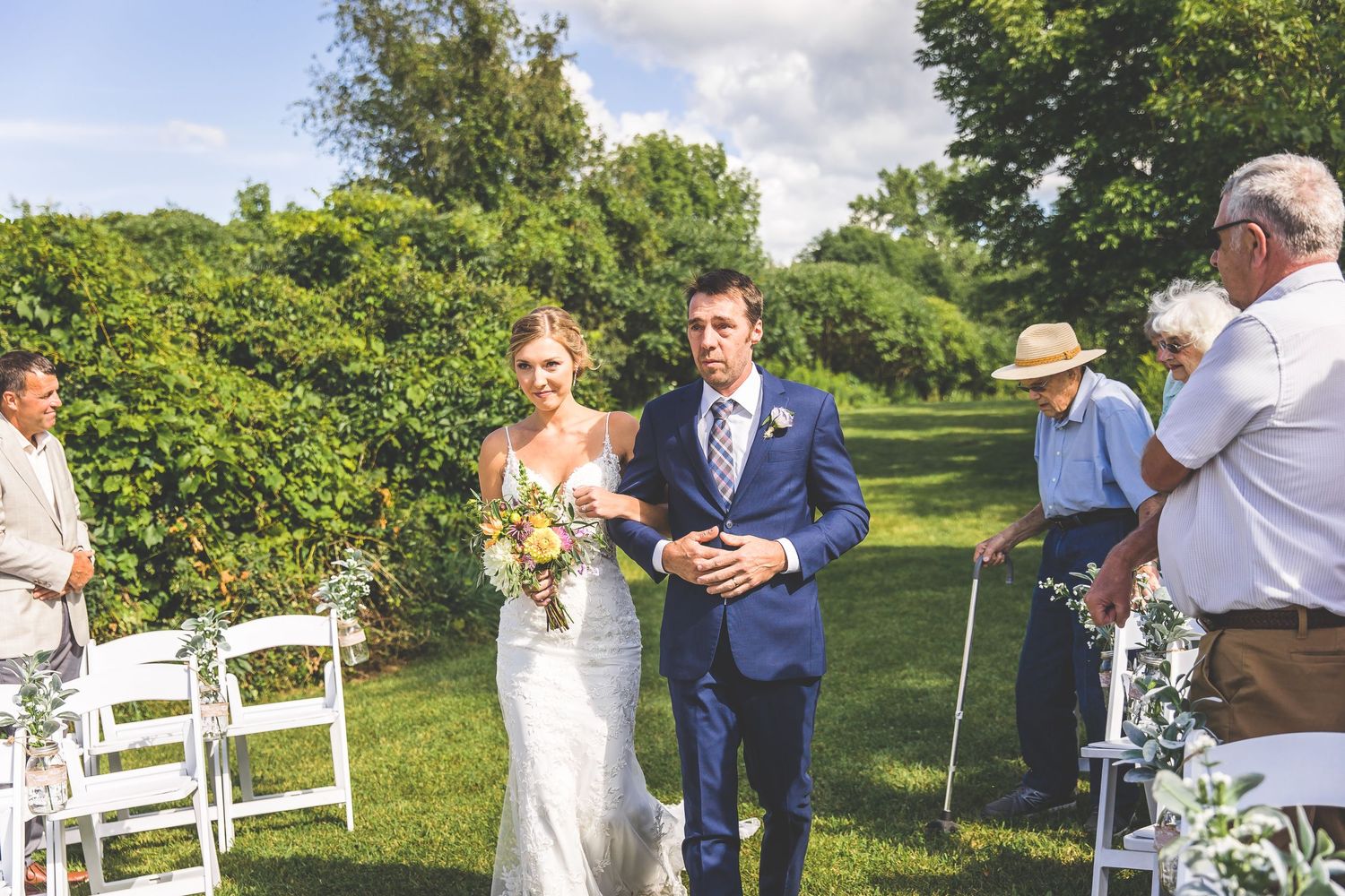 White chairs and floral decorations set up for an outdoor garden wedding ceremony.