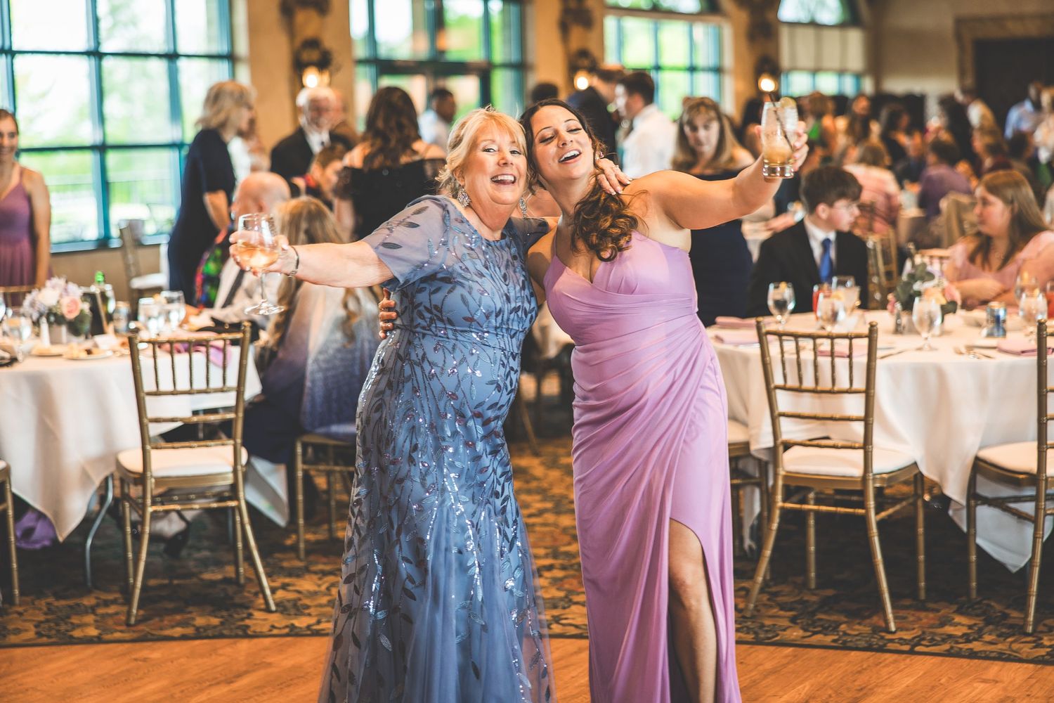 Wedding guests in elegant dresses dancing and celebrating at an indoor reception.