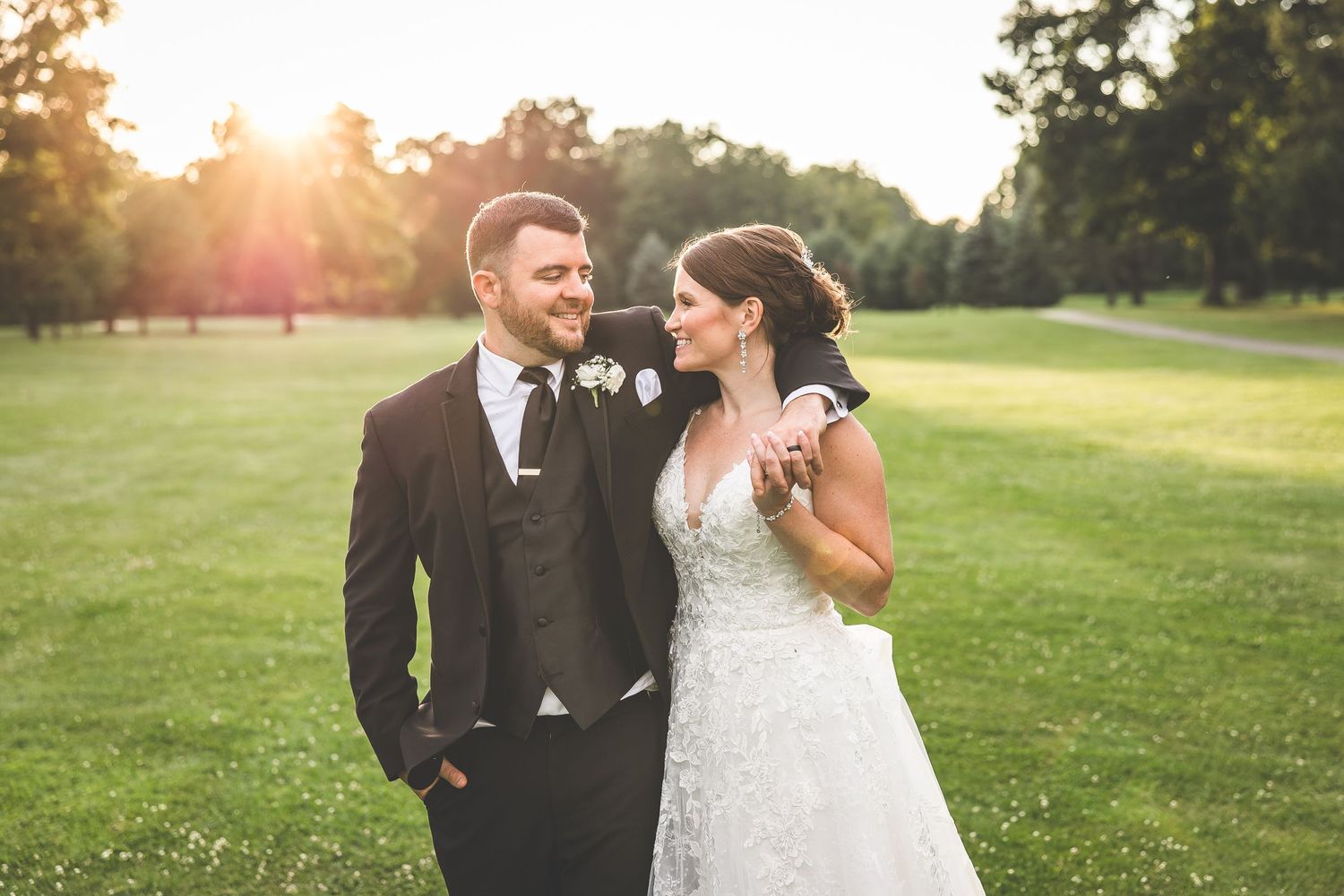 Romantic wedding couple embraces on a sun-drenched golf course at golden hour.